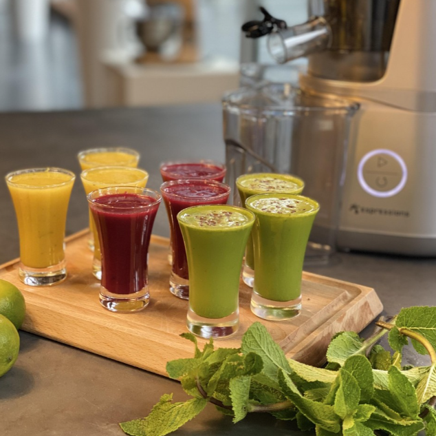 Glasses with mixed color juices on a wooden tray with mint and a juicer.