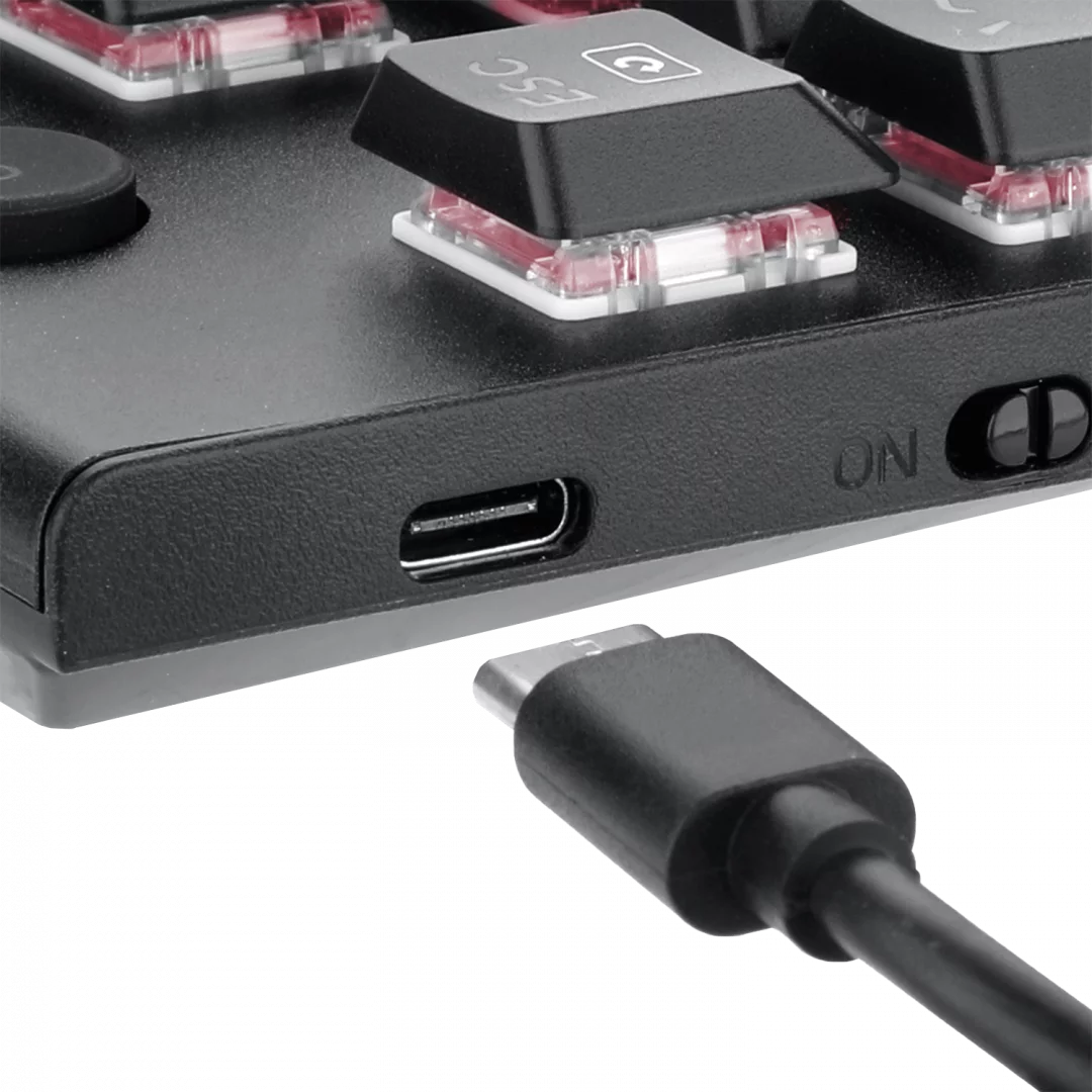 Közelkép egy fekete billentyűzetről USB-C porttal és bedugott kábellel, a bekapcsoló gomb bekapcsolt állásban.