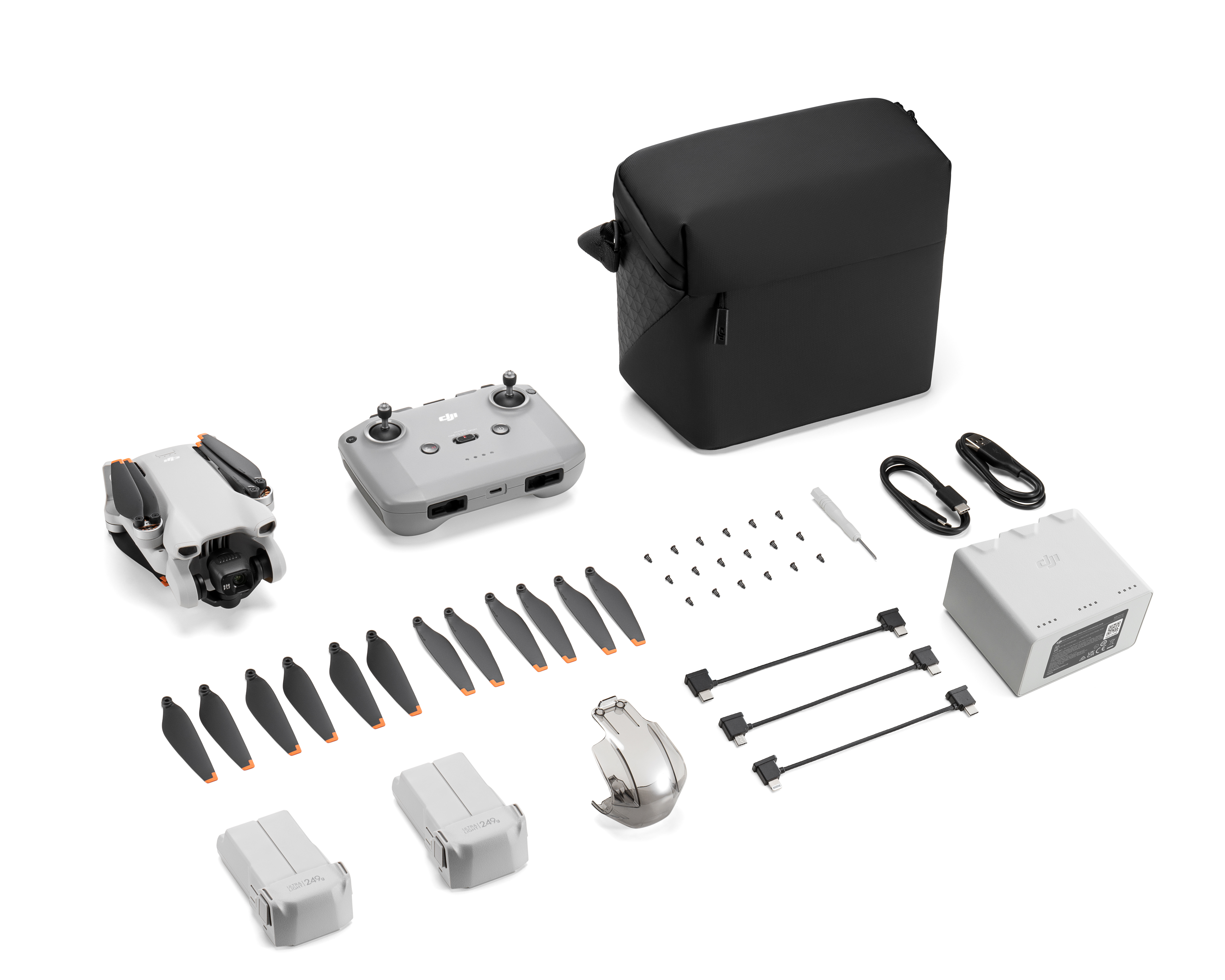 Kit de dron con dron, controlador, hélices, baterías y una funda, todo sobre una superficie blanca.