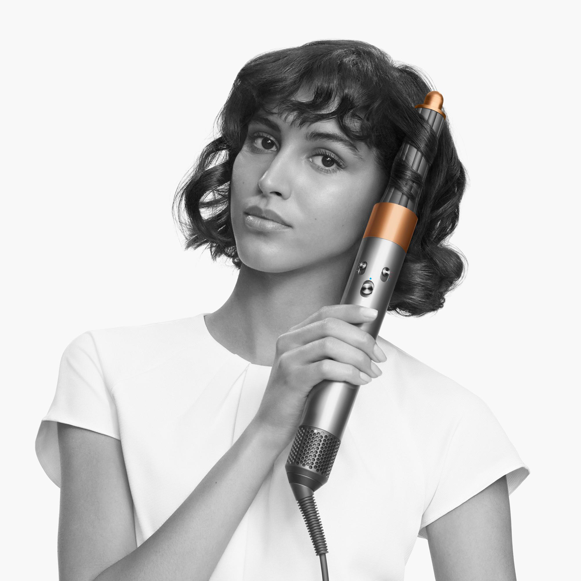 Frau mit einem Haarstyling-Werkzeug. Sie hält das Werkzeug und schaut in die Kamera.