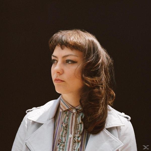 Eine Frau mit braunem Haar, die zur Seite blickt, trägt eine weiße Jacke und ein gestreiftes Hemd.