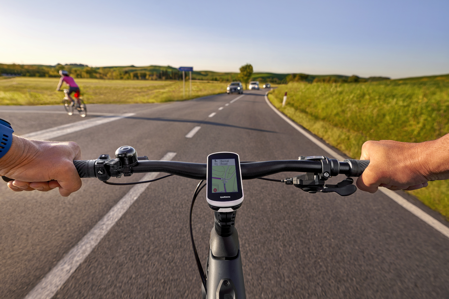 First-person view of cyclist on road with Garmin device on handlebars.
