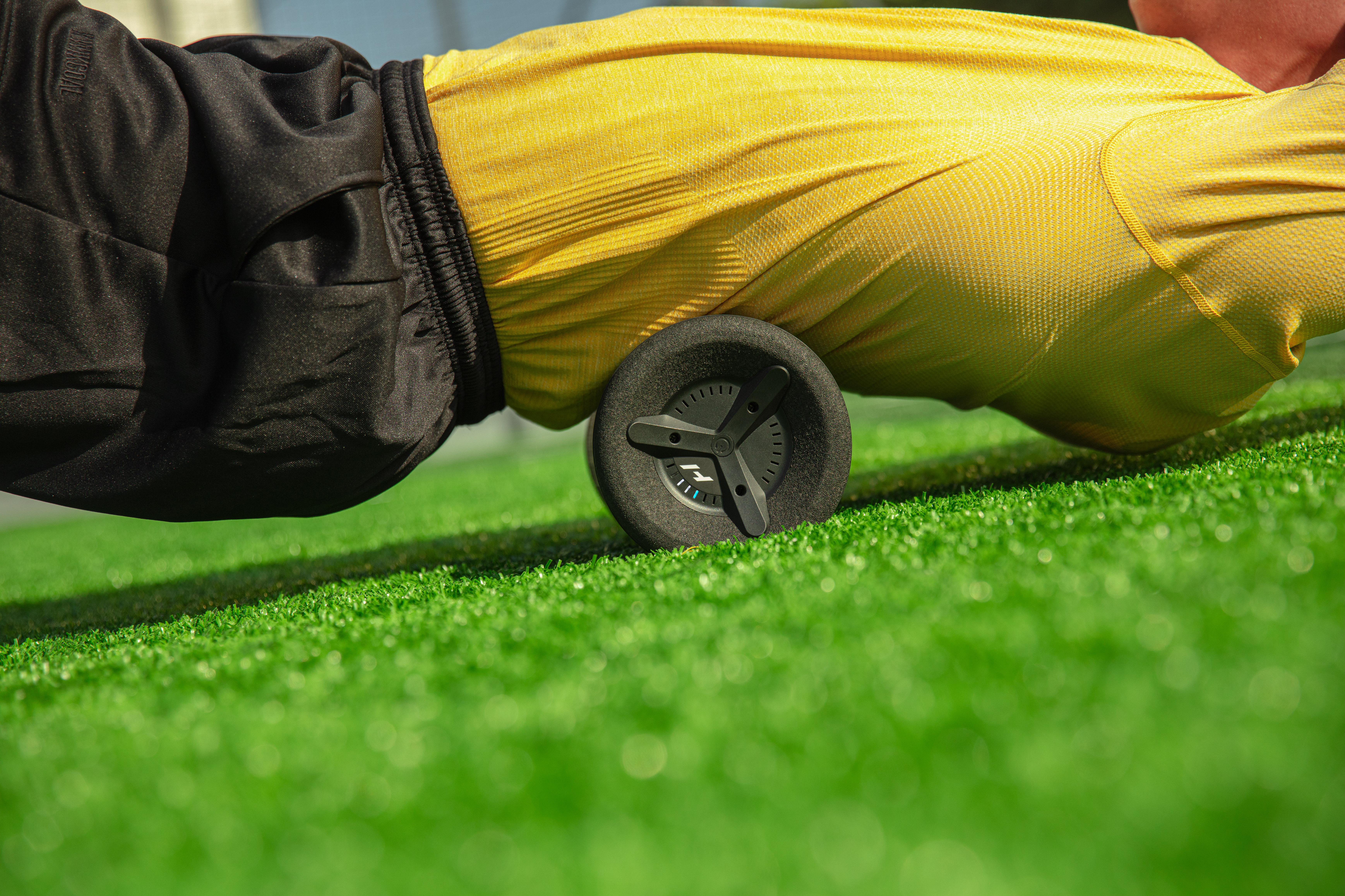 Person liegt auf Gras, verwendet eine schwarze Faszienrolle für die Rückenmassage.