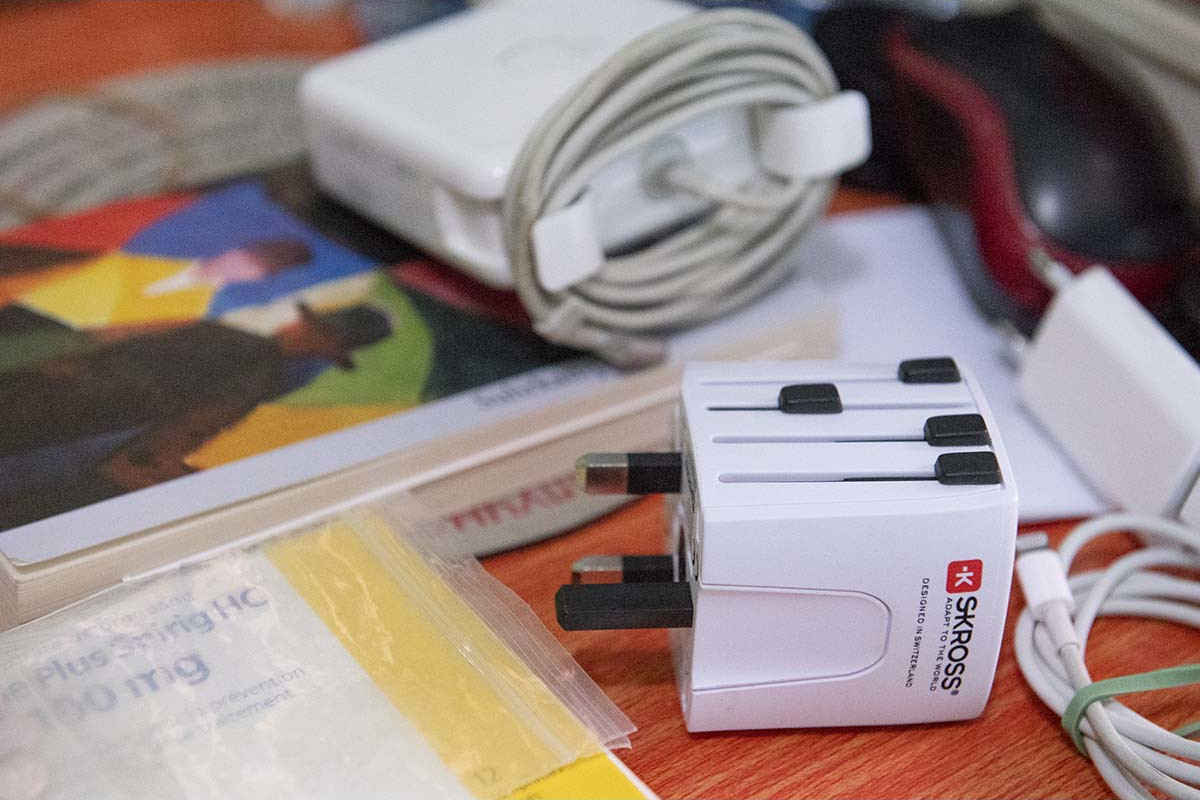 Divers objets sur une table : un adaptateur secteur blanc avec un cordon enroulé, un livre et un adaptateur multiple.
