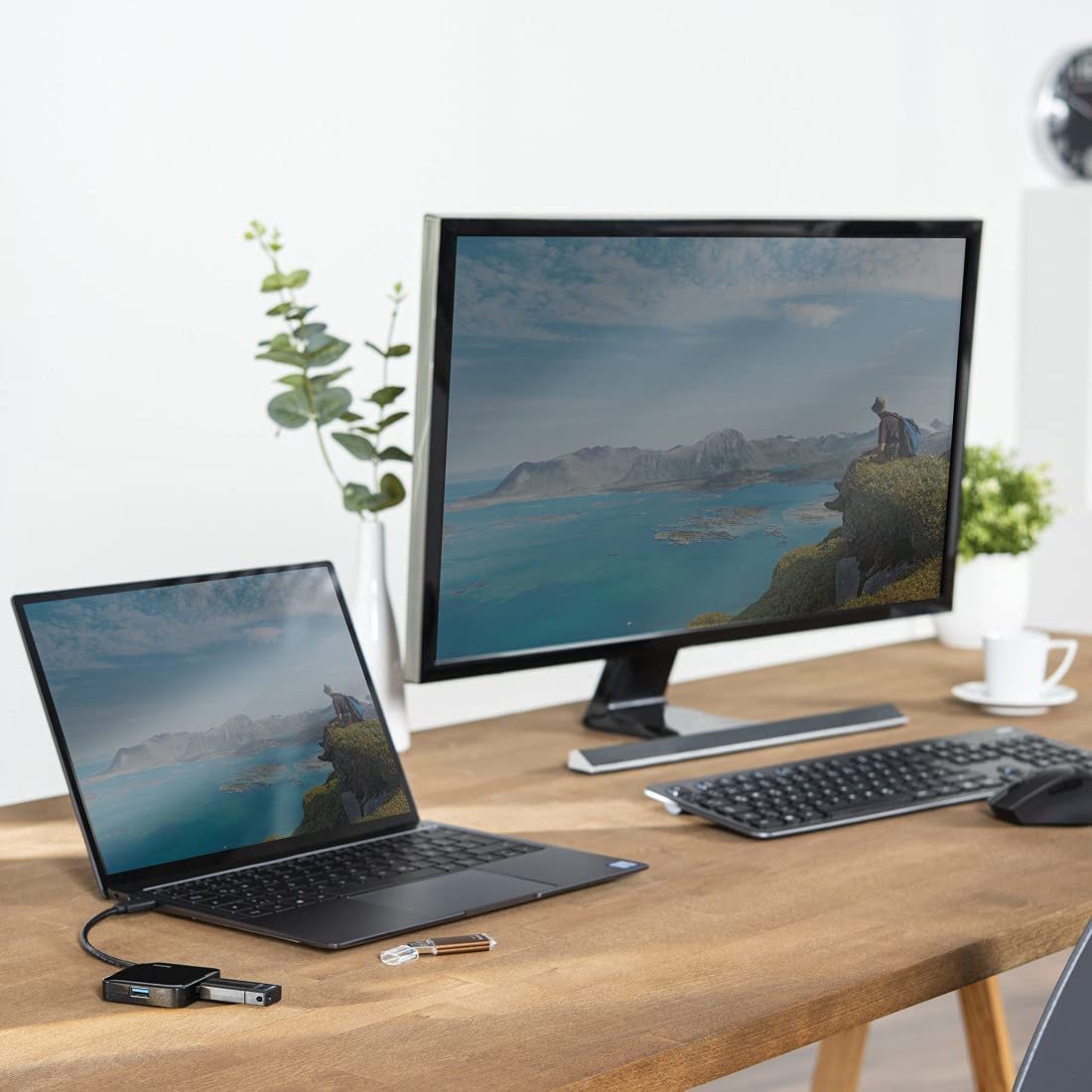 Laptop, monitor, billentyűzet és egér egy faasztalon.