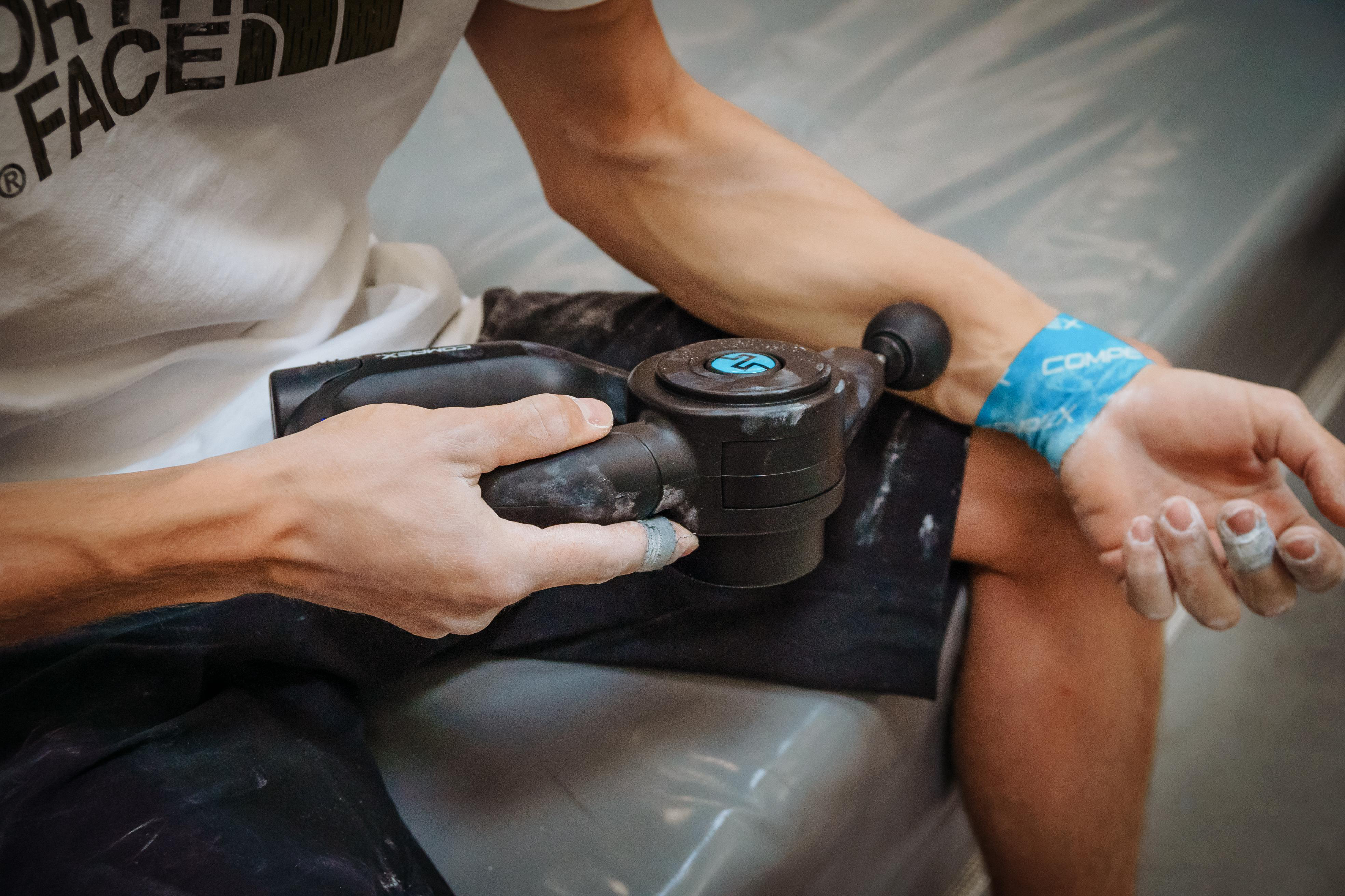 Person, die eine Massagepistole an ihrem Arm benutzt.