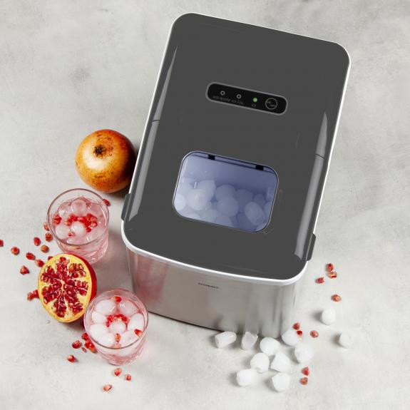 An ice maker with ice cubes in the window and a pomegranate on the counter.