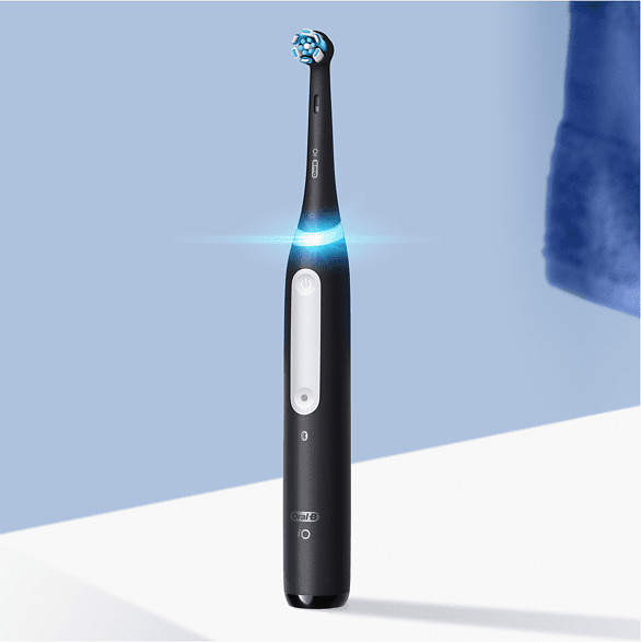 Brosse à dents électrique Oral-B iO noire, illuminée, sur fond blanc et bleu.