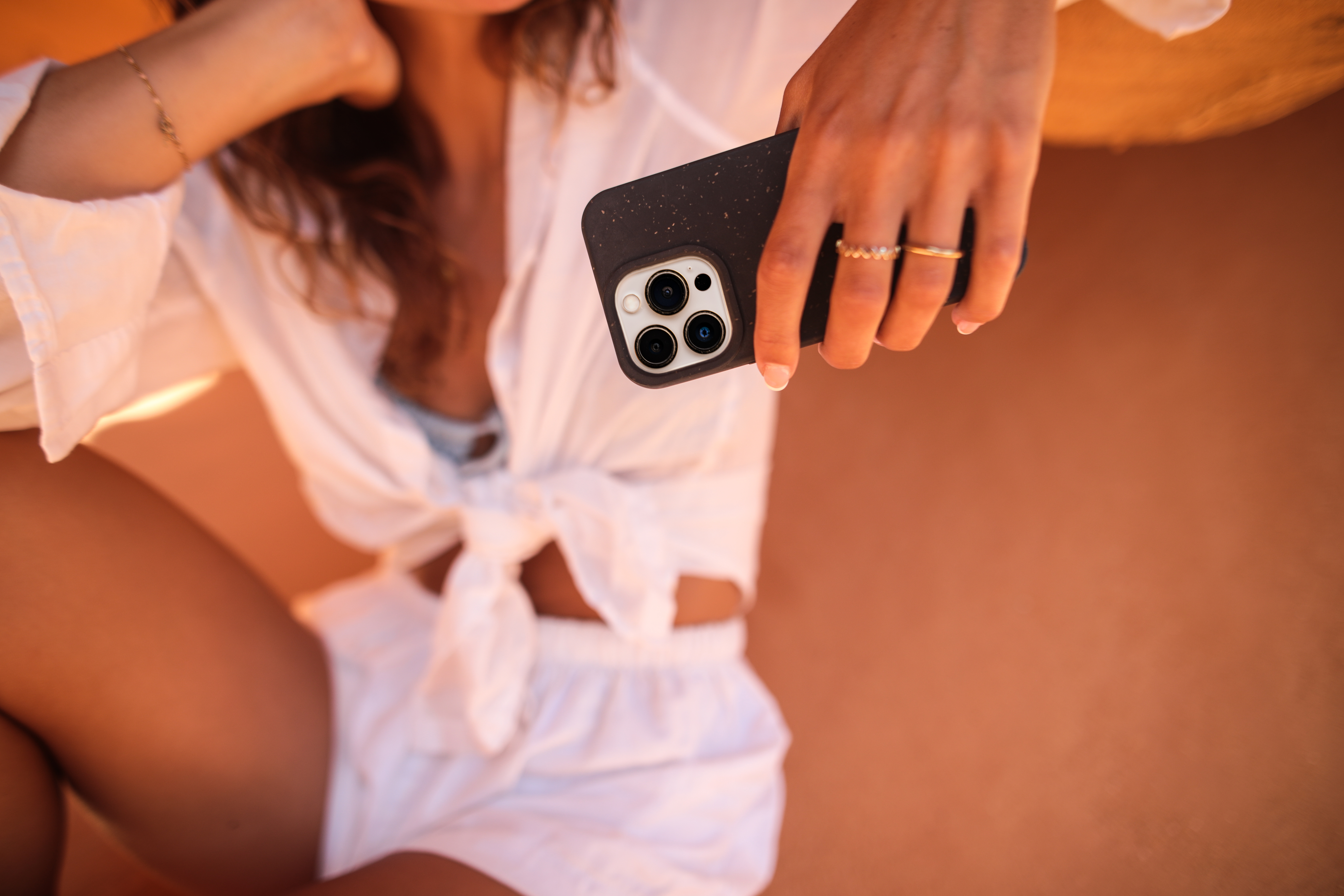 Eine Frau hält eine schwarze Telefonhülle mit einer Kamera. Sie trägt ein weißes Hemd und Shorts, Nahaufnahme.