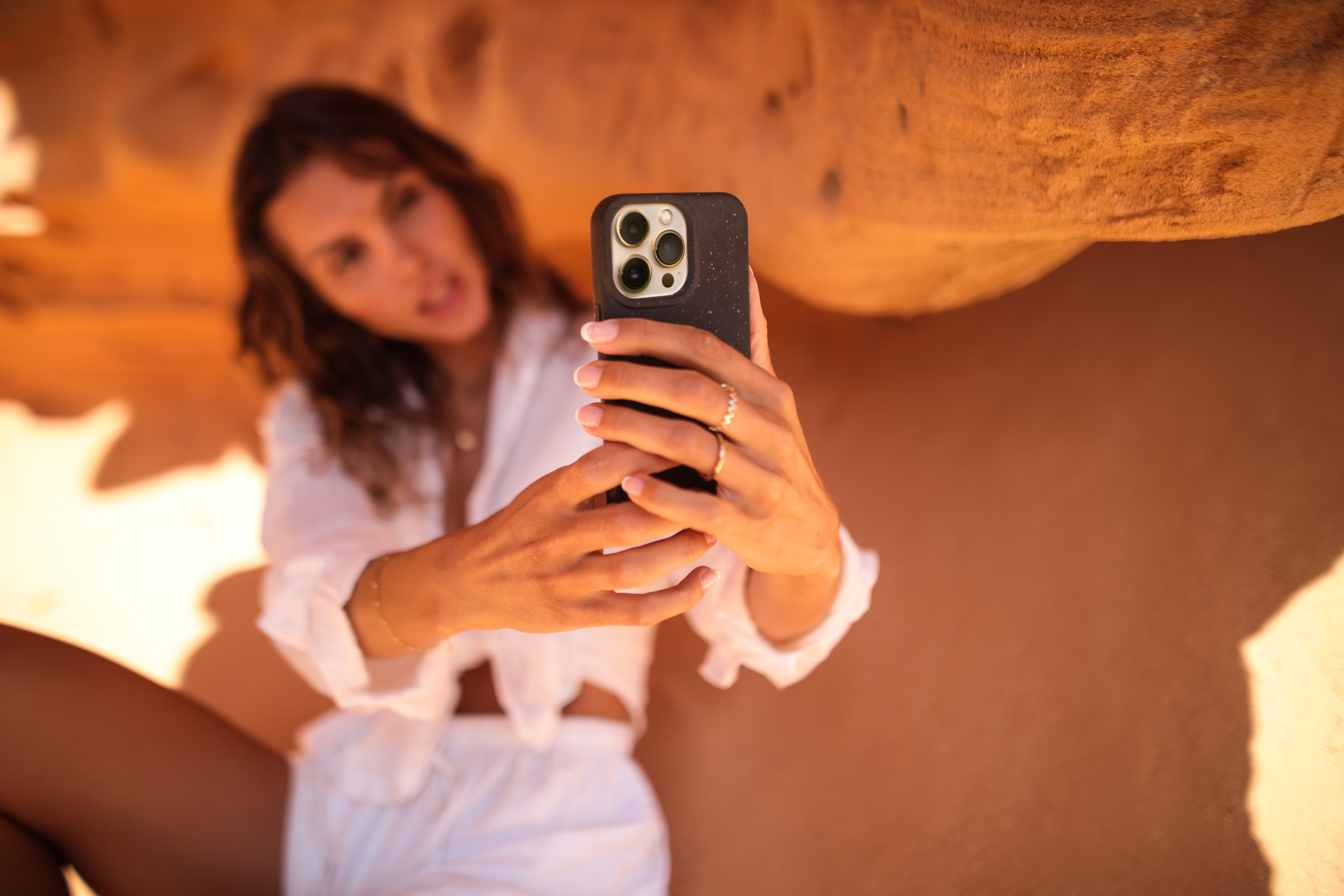 Frau macht Selfie mit iPhone, trägt weiße Kleidung, in einer wüstenartigen Landschaft.