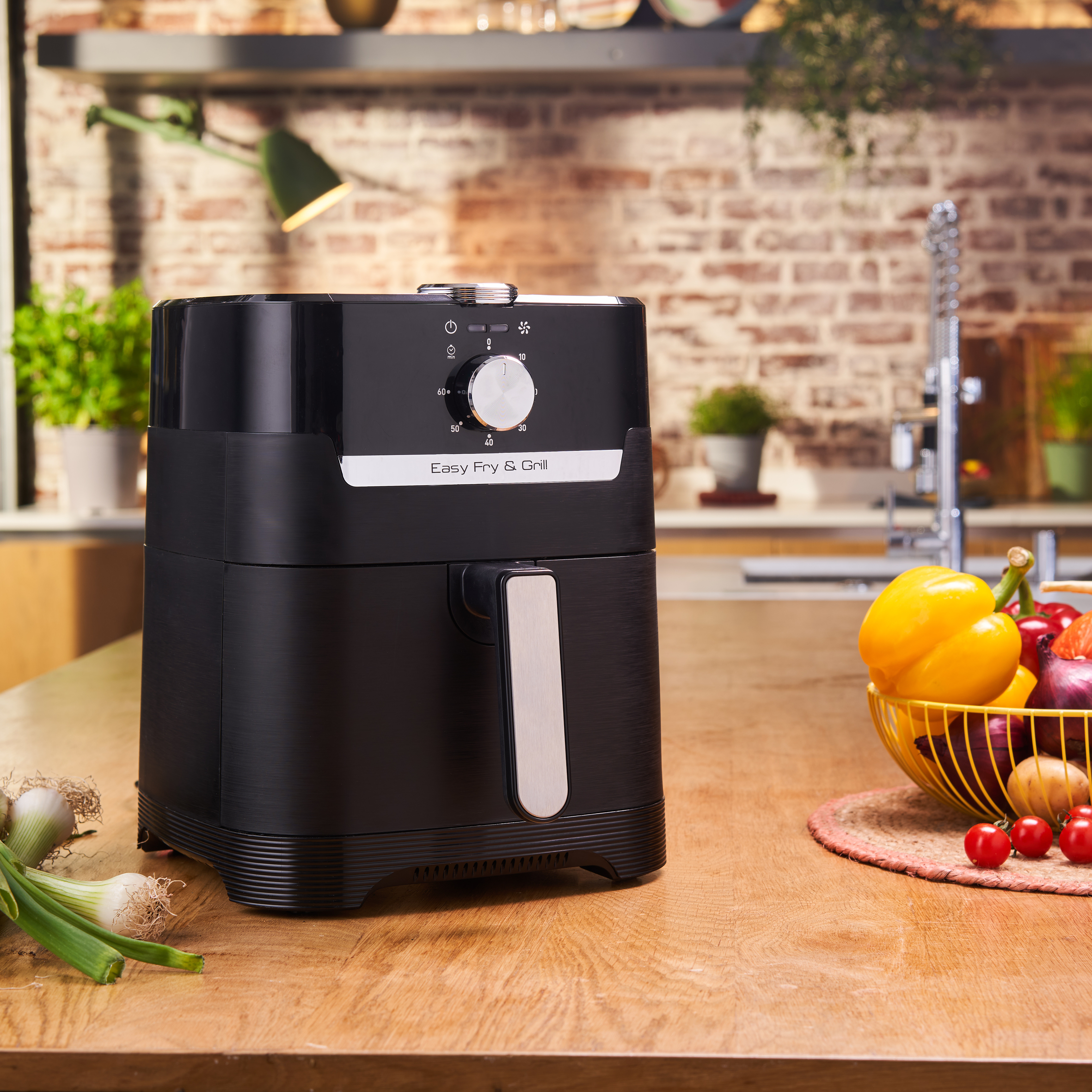 Friteuse à air noire sur un comptoir en bois avec des légumes.