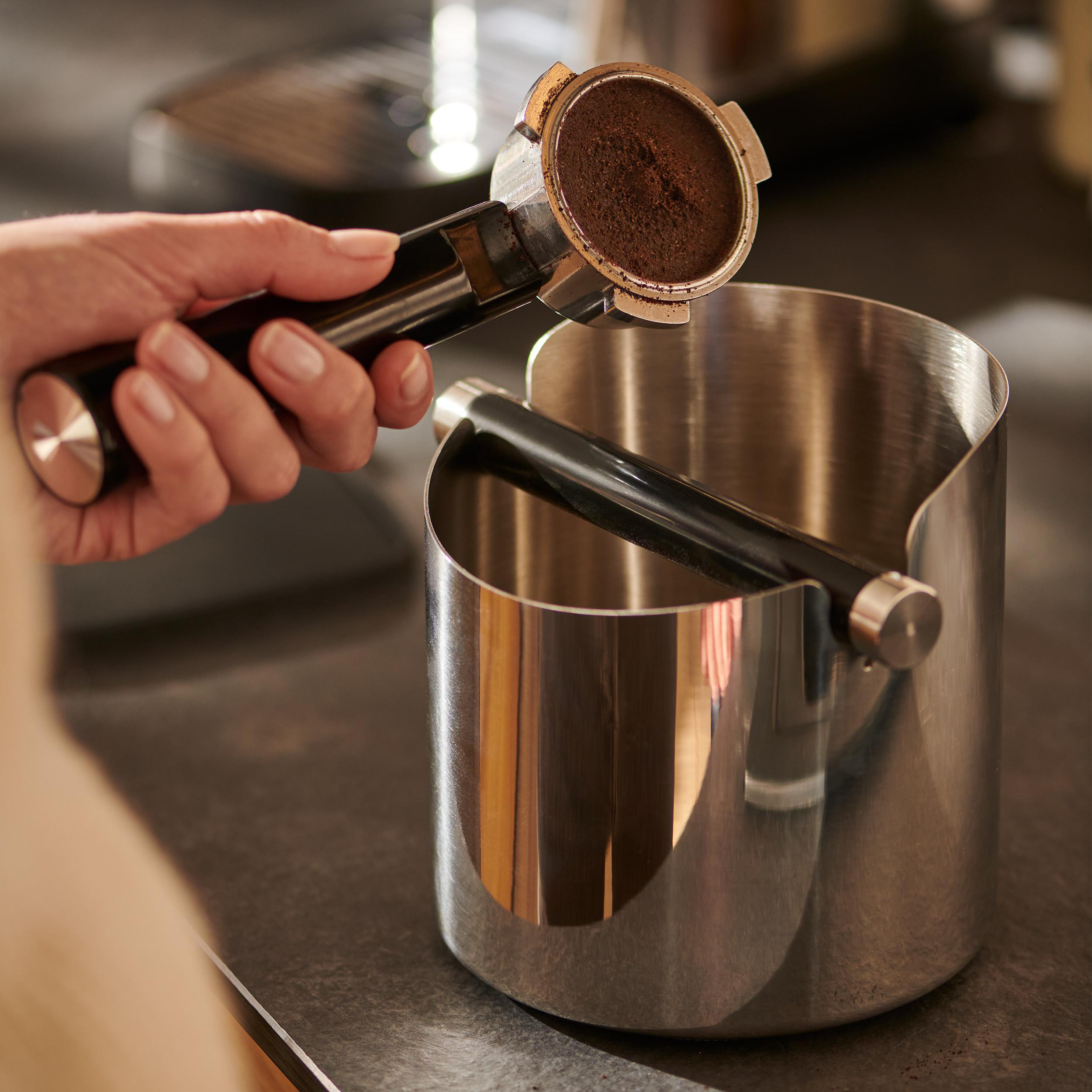Hand hält einen Siebträger mit Kaffeesatz über einer Abschlagbox.