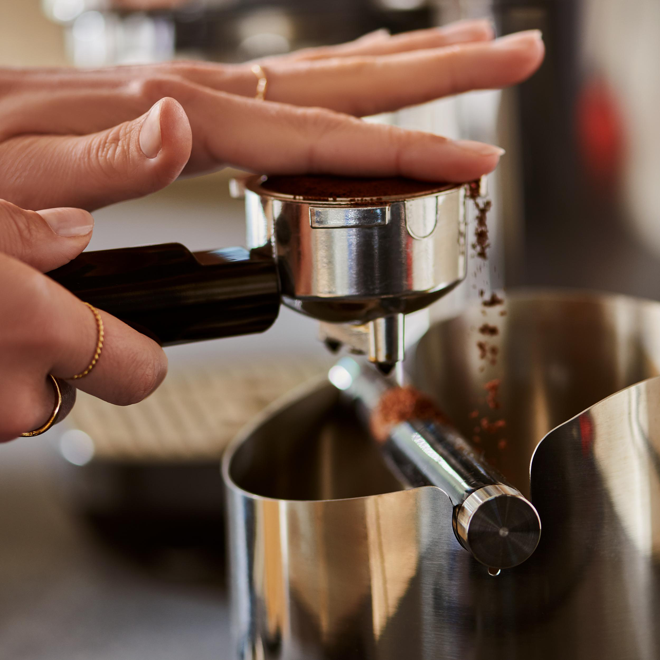 Hände drücken Kaffeepulver in einen Siebträger.
