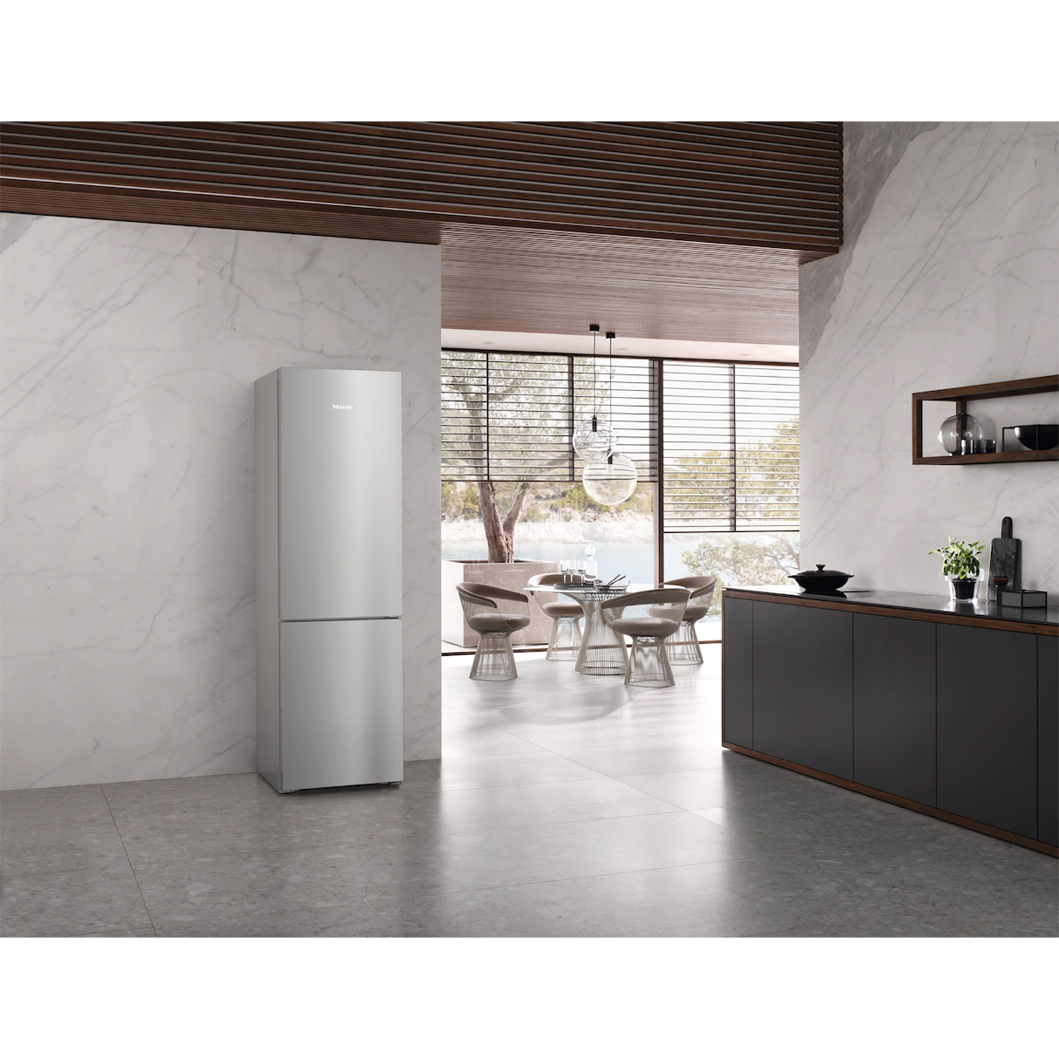 Una cucina moderna con frigorifero argentato. Una zona pranzo è visibile attraverso un arco. Muri in marmo e armadi scuri.