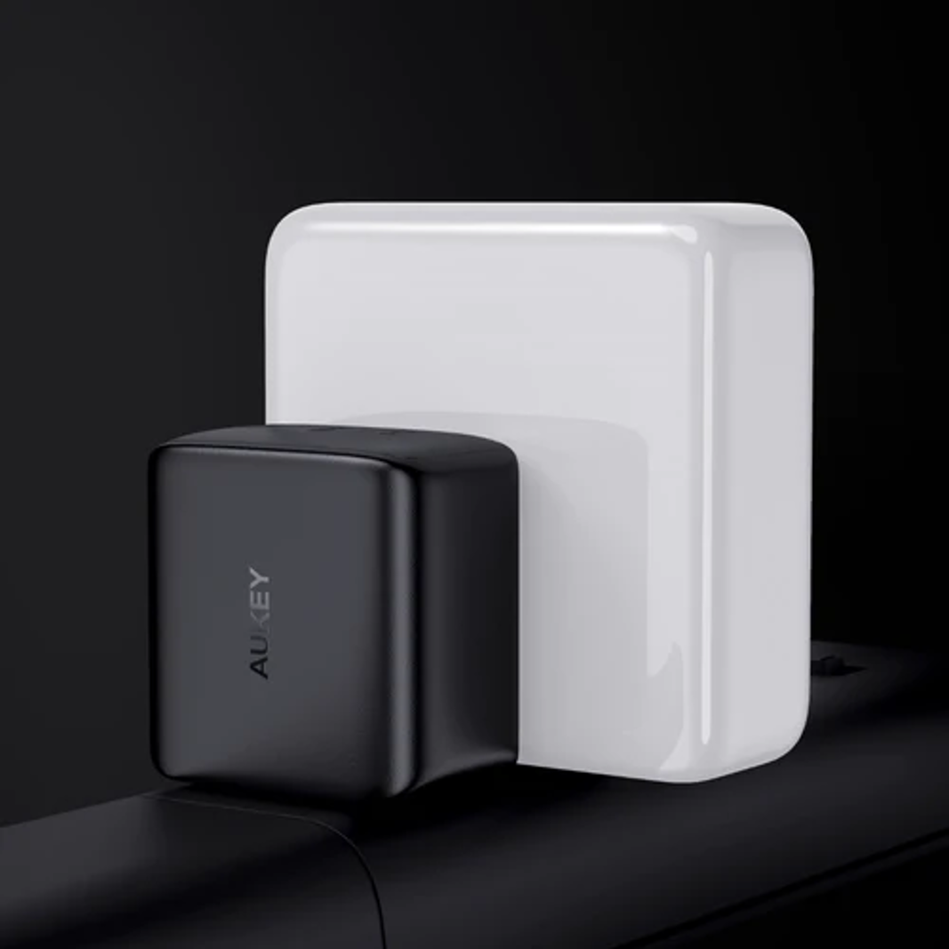 Caricatore AUKEY in bianco e nero. Un piccolo caricatore a cubo collegato a un cubo bianco.