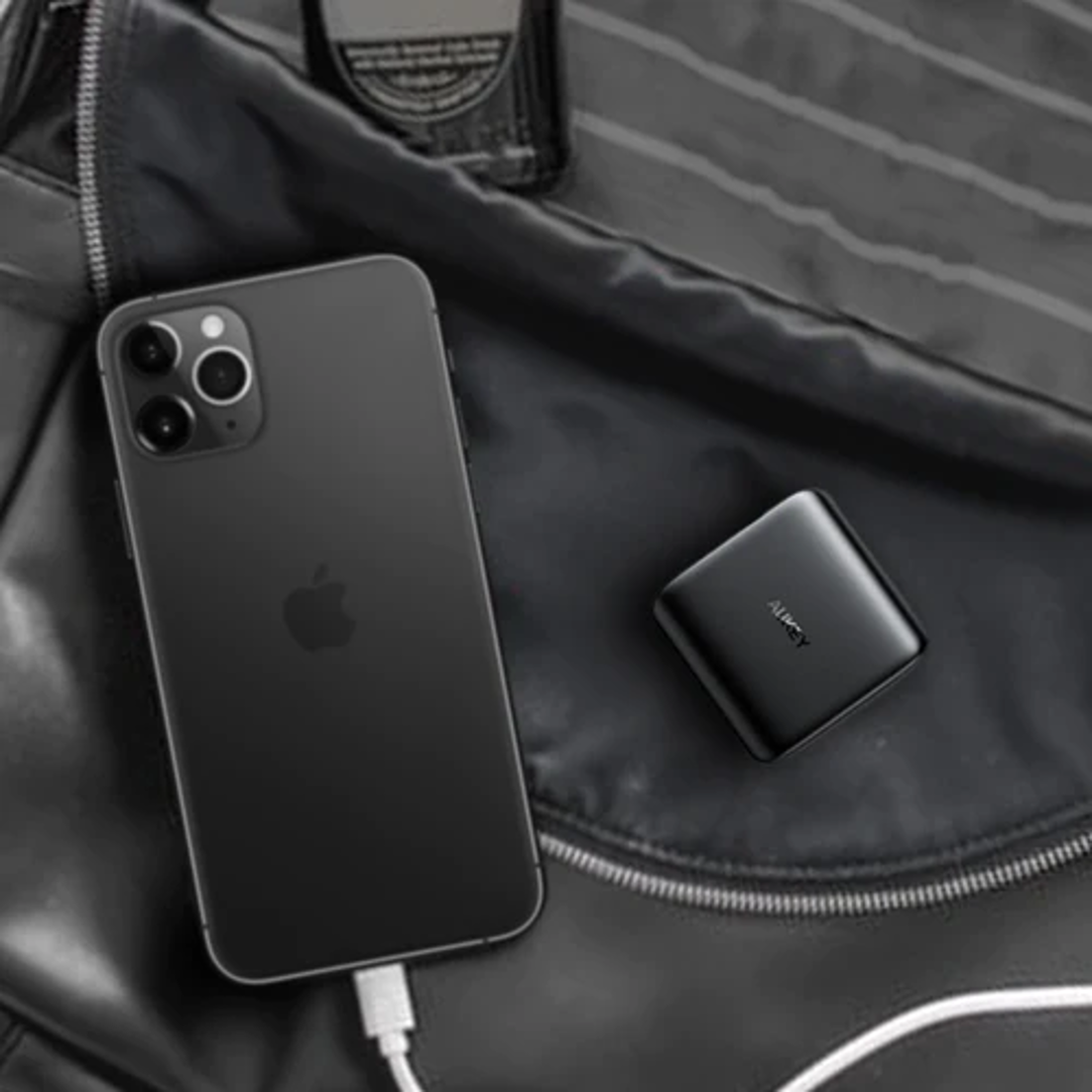 iPhone nero collegato al caricabatterie, accanto a un caricabatterie Aukey nero, su una borsa nera.