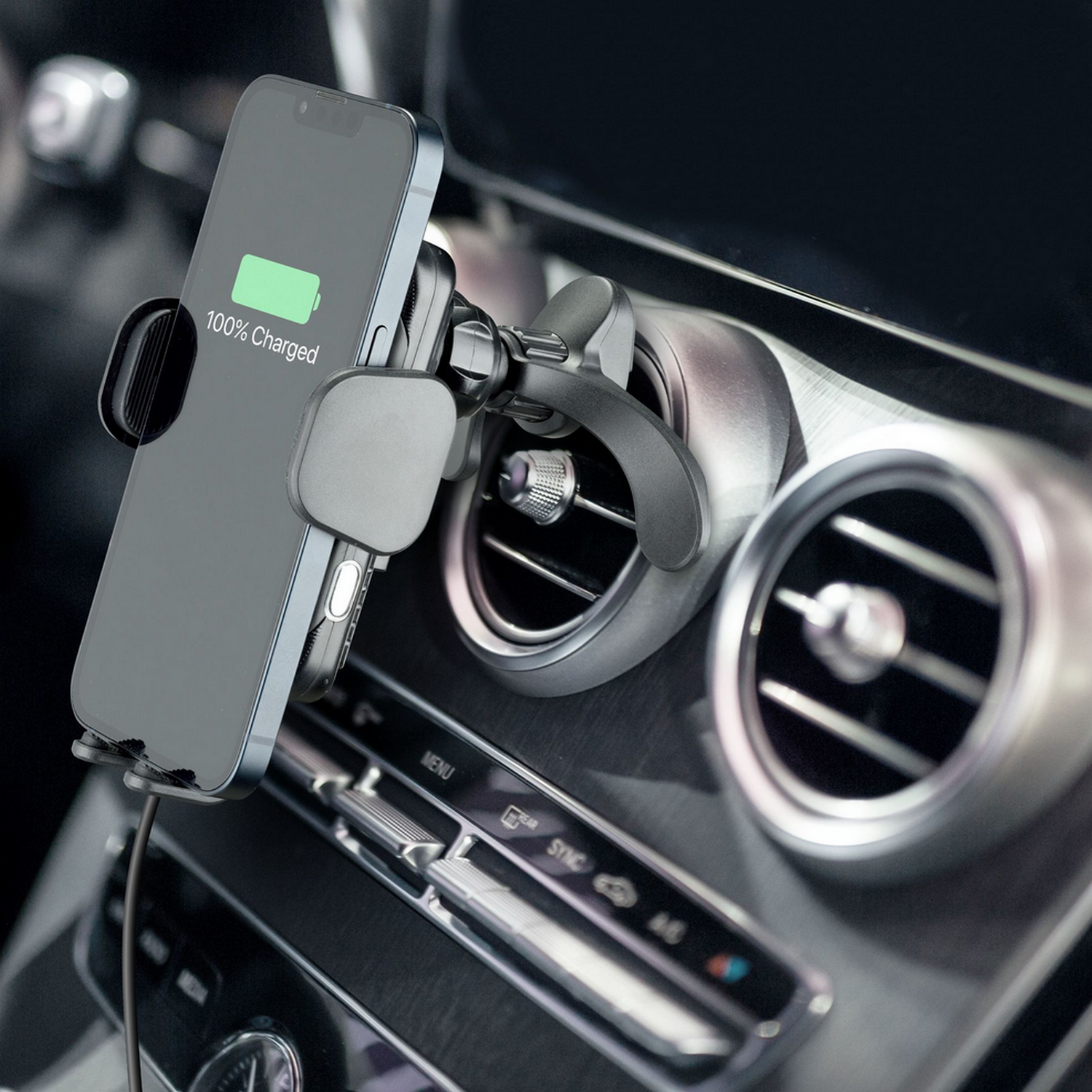 Phone mounted on car vent, charging. Screen shows 100% charged. Car interior.