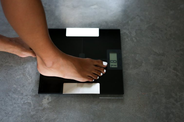 Le pied d'une personne sur une balance numérique noire, avec le poids affiché.