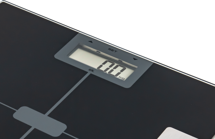 Une balance numérique affiche '0,0 kg'. La balance est noire avec des accents gris. Fond noir.