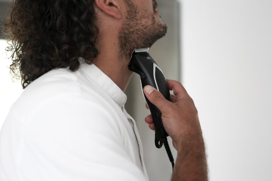 Homme taillant sa barbe avec une tondeuse électrique, plan rapproché.