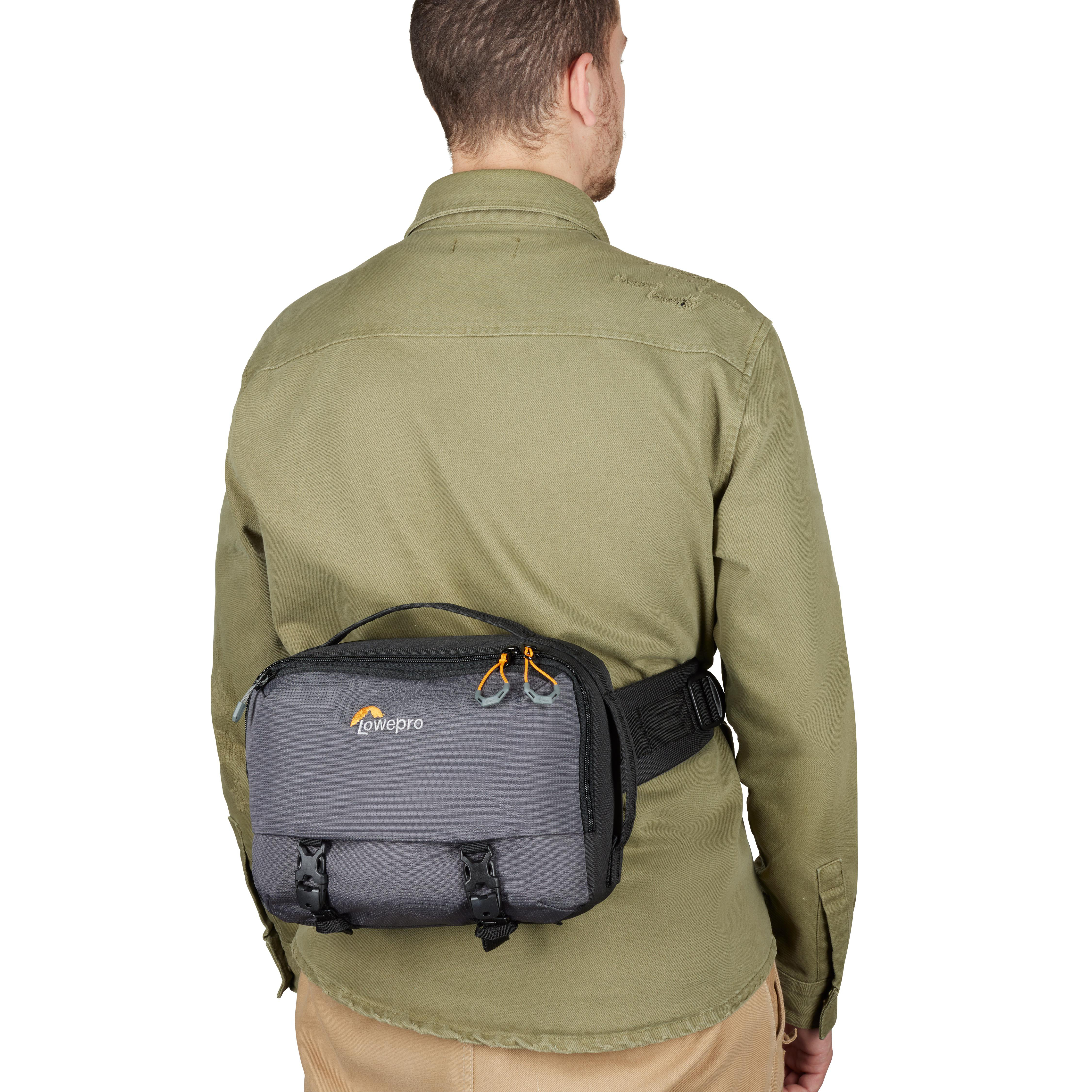 Ein Mann mit grünem Hemd trägt eine graue Kameratasche um die Taille. Die Tasche hat ein Lowepro-Logo.