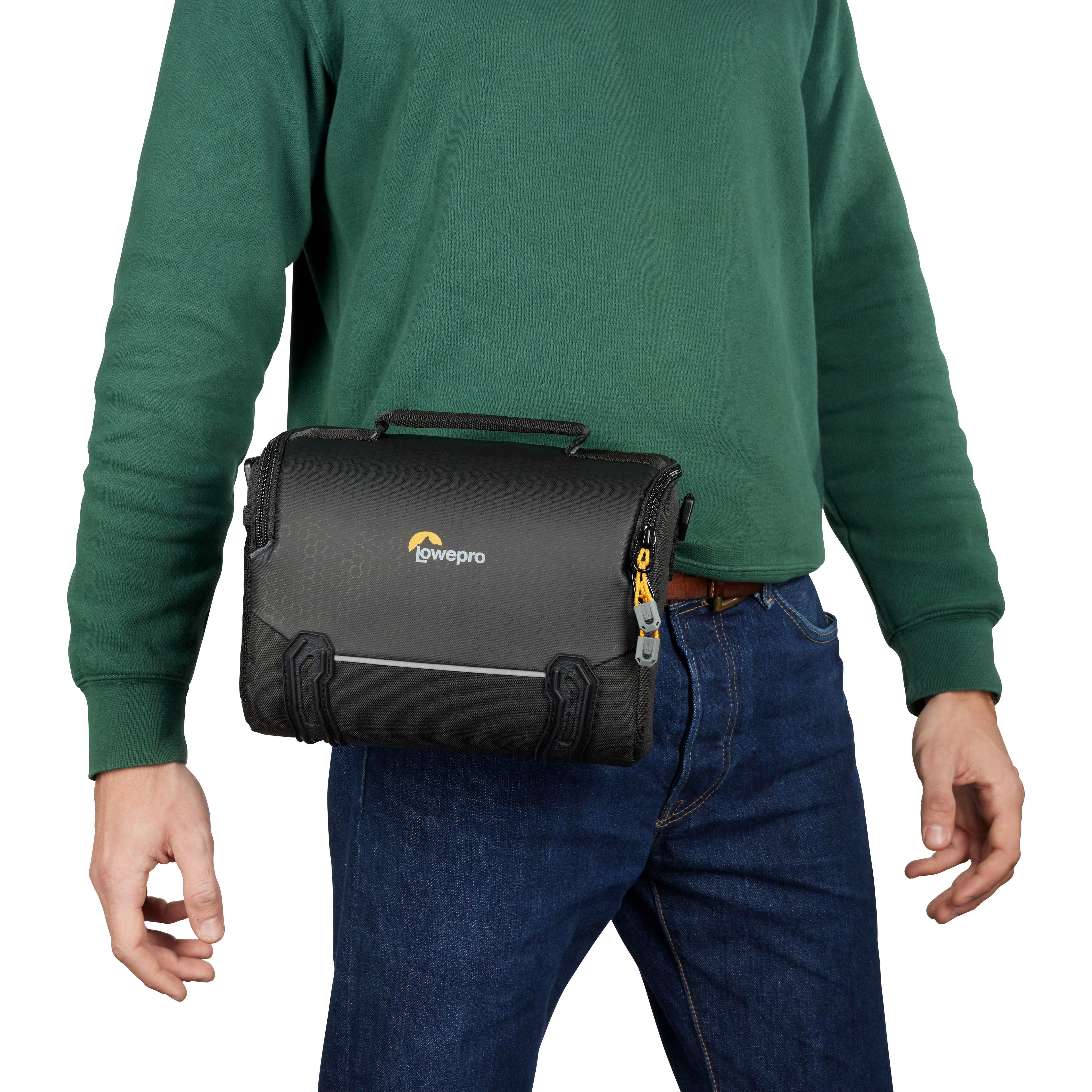 Mann trägt grünes Hemd und Jeans und trägt eine schwarze Lowepro-Kameratasche um die Taille.