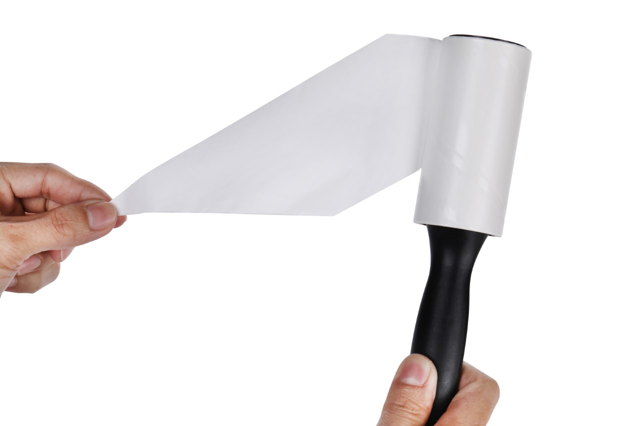 Mano sosteniendo un rodillo quitapelusas quitando una hoja de papel adhesivo usado.