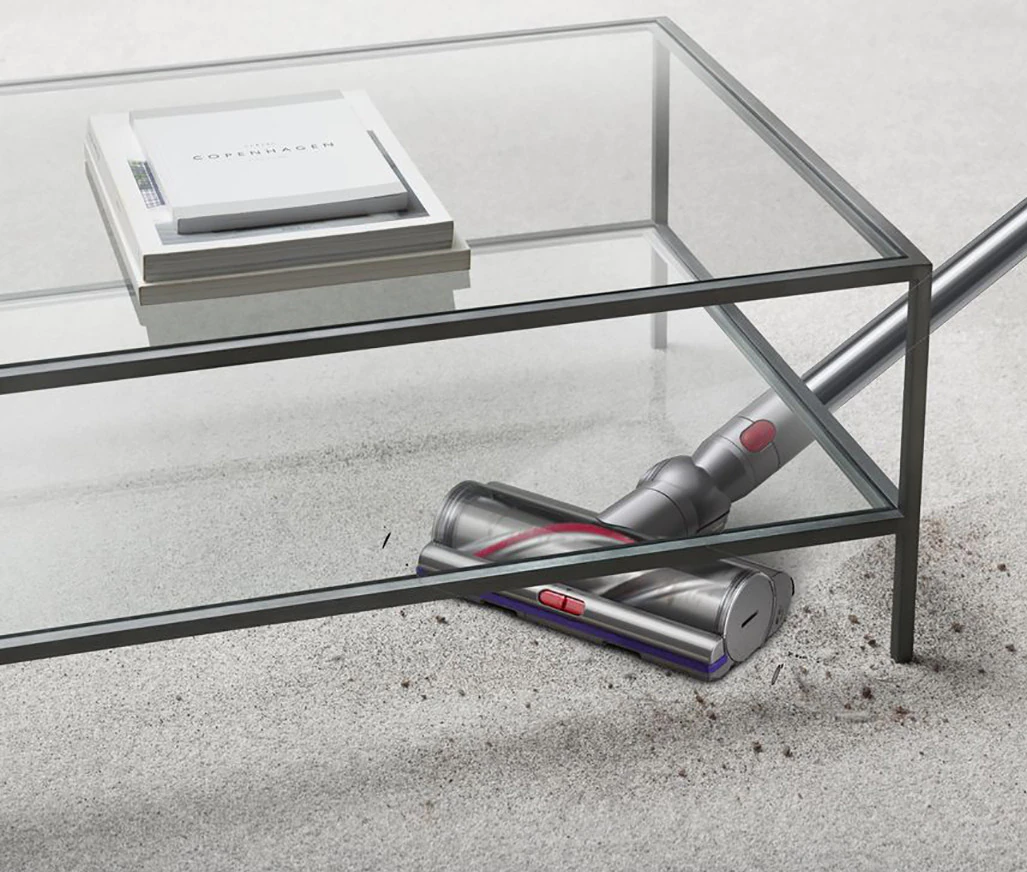 Cabezal de aspiradora en un suelo claro, debajo de una mesa de vidrio.