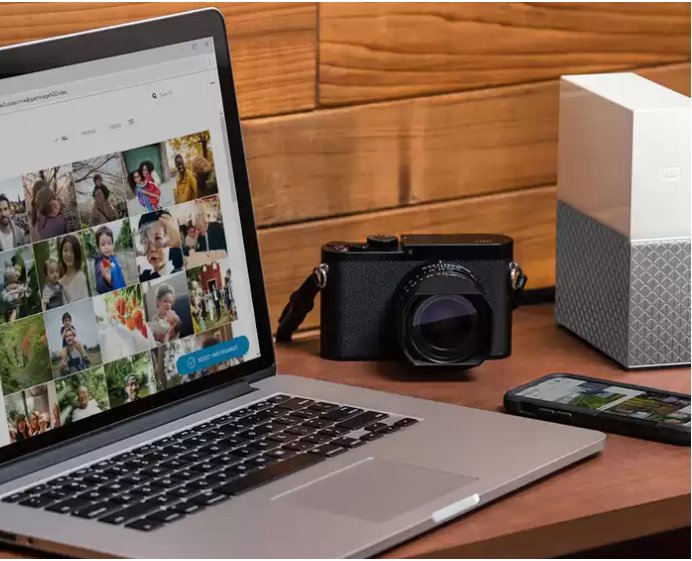Laptop, fotocamera, telefono e disco rigido su una scrivania di legno. Foto di famiglia sullo schermo.