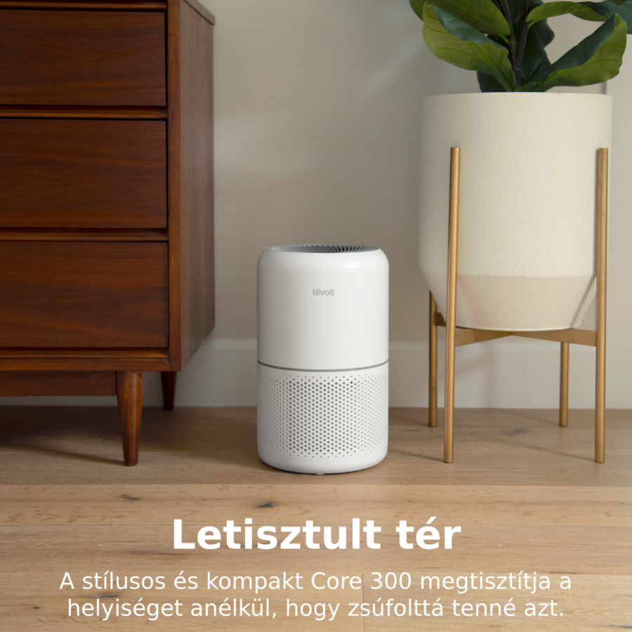 Légtisztító a fapadlón, egy komód és egy fehér cserépben lévő növény mellett.