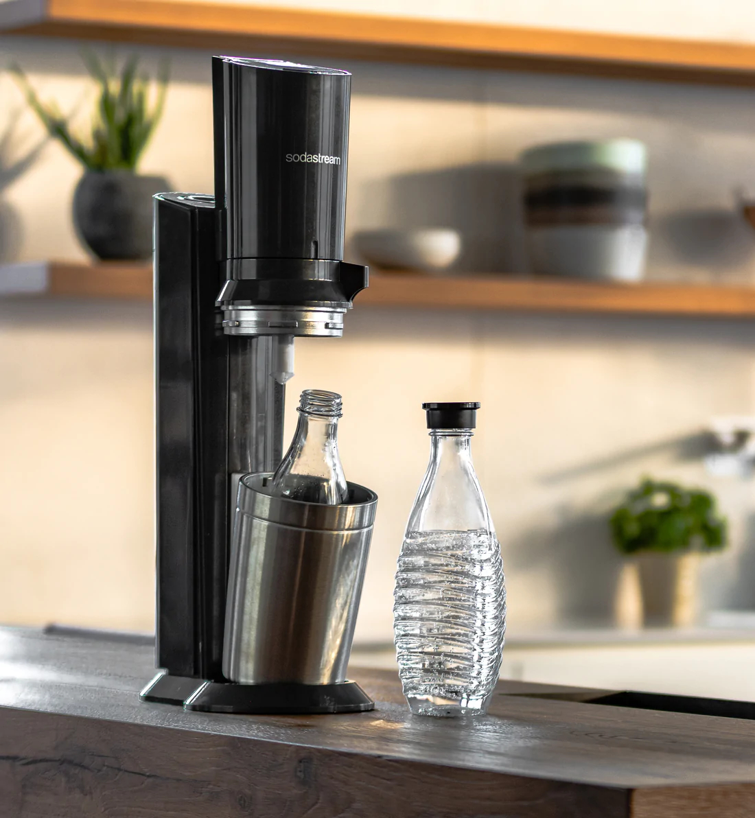 SodaStream-Maschine mit Flasche, und eine gefüllte Flasche daneben. Küchenhintergrund.