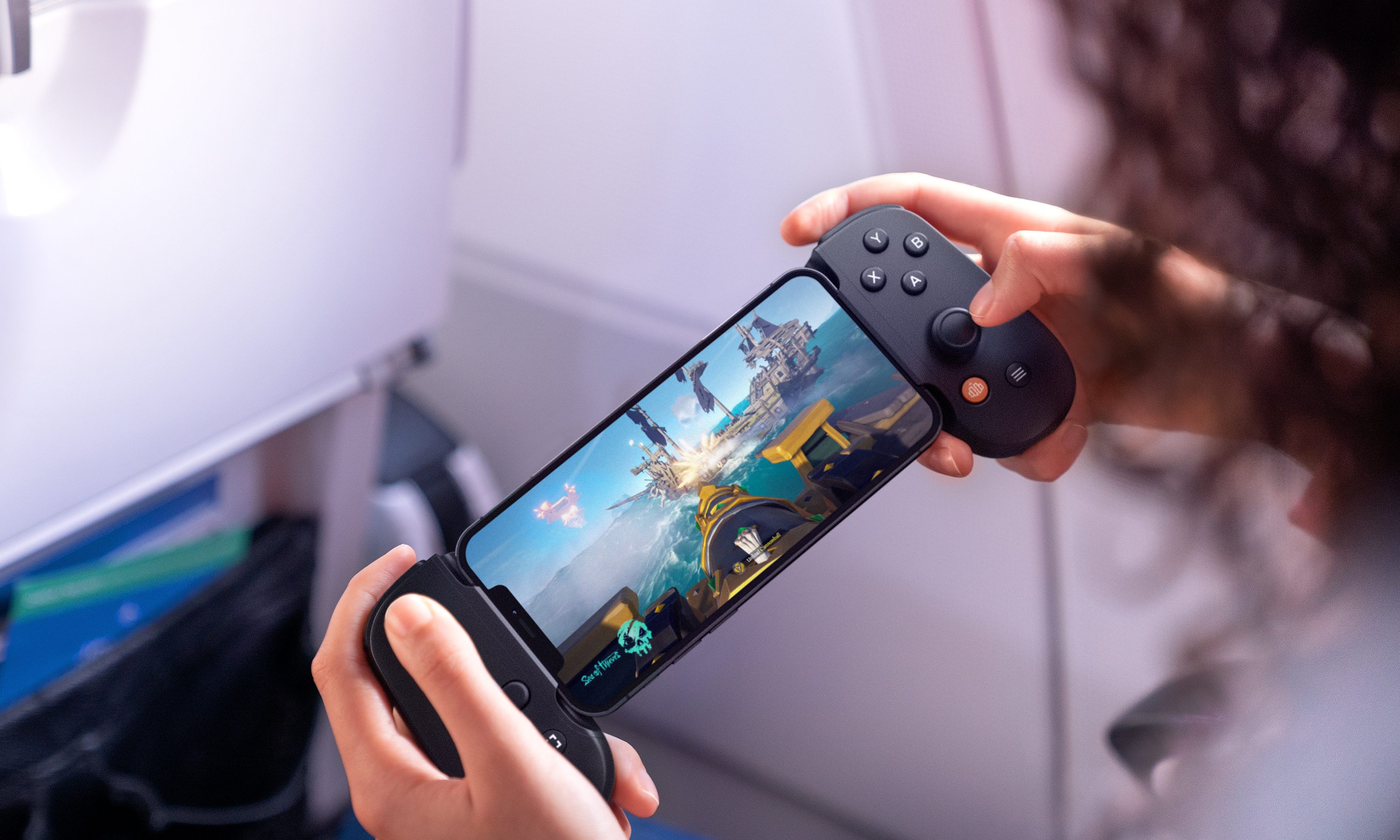 Person hält ein Telefon mit Controller. Spielbild zeigt Piratenschiff-Schlacht.