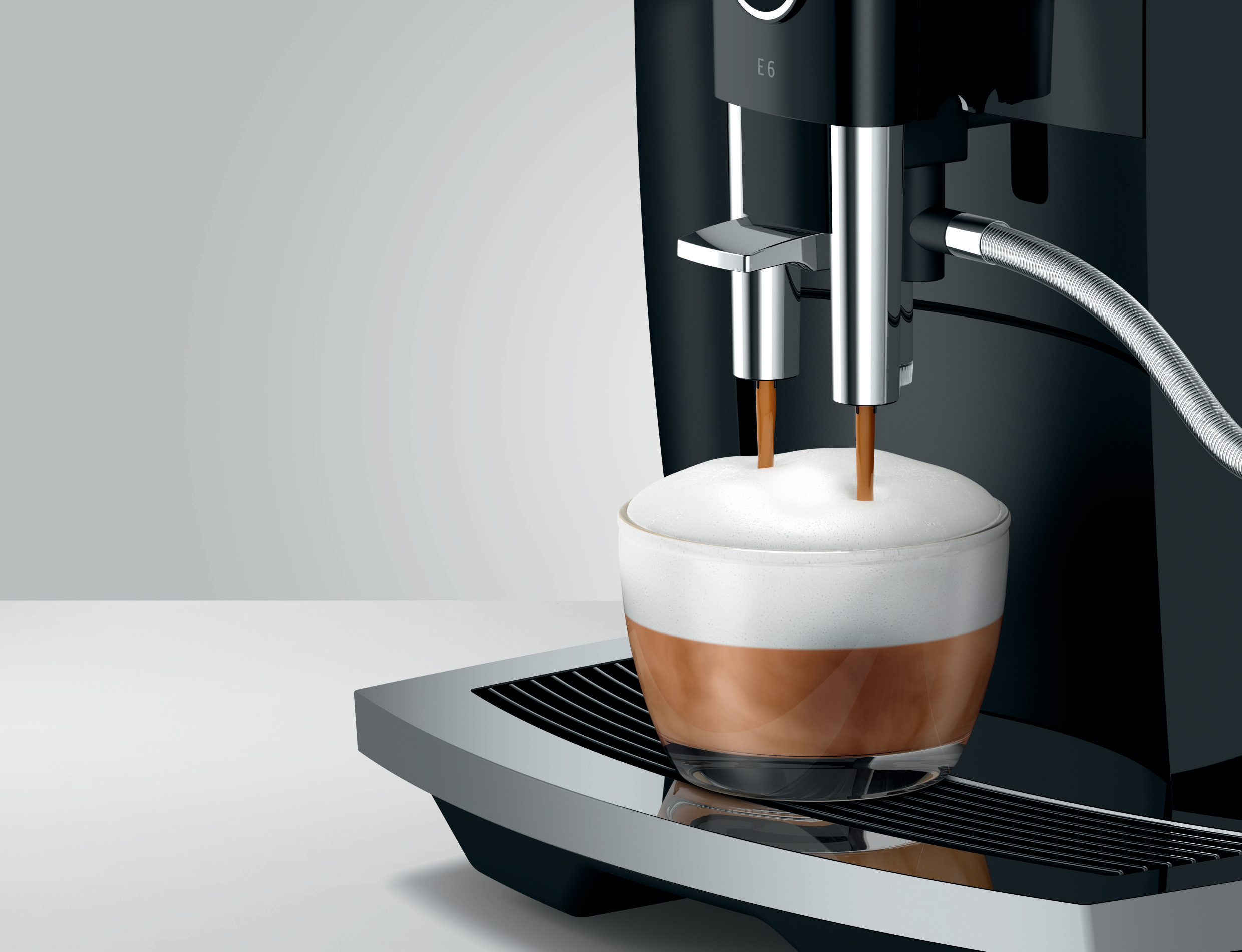 Espressomaschine gibt Kaffee in ein Glas mit Milchschaum obenauf aus.