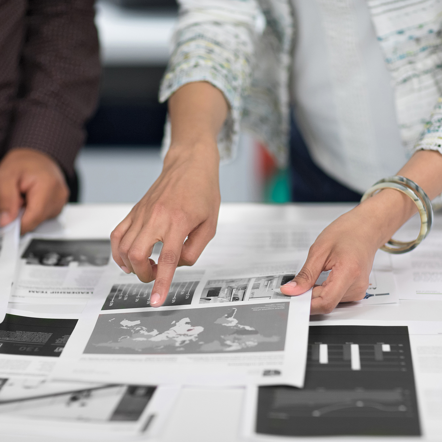 Deux personnes, l'une pointant vers une carte du monde en noir et blanc. Des papiers avec des graphiques sont visibles.