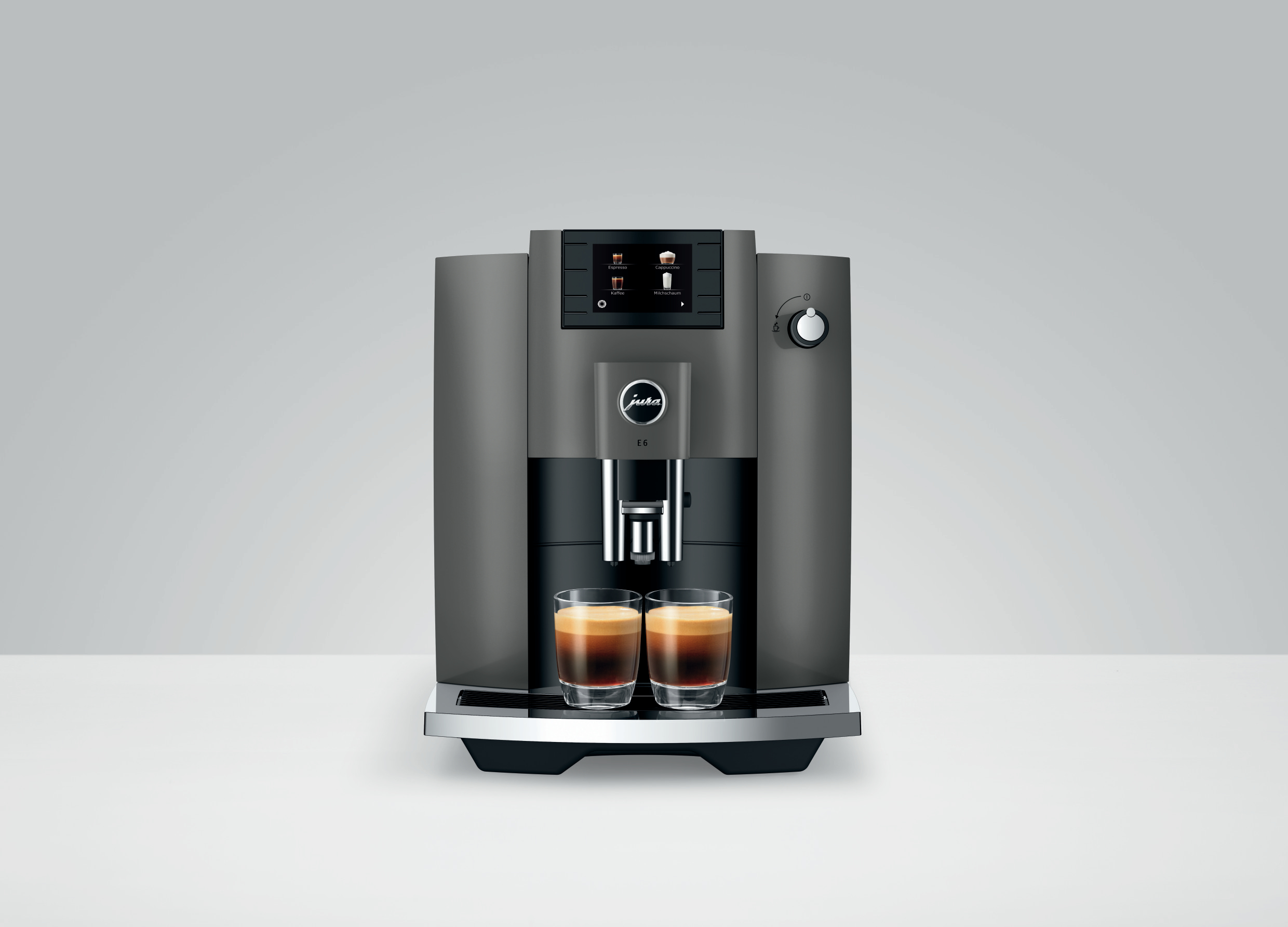 Eine dunkelgraue Jura Kaffeemaschine. Sie hat ein Display, einen Drehregler und zwei Kaffeegläser auf der Theke.