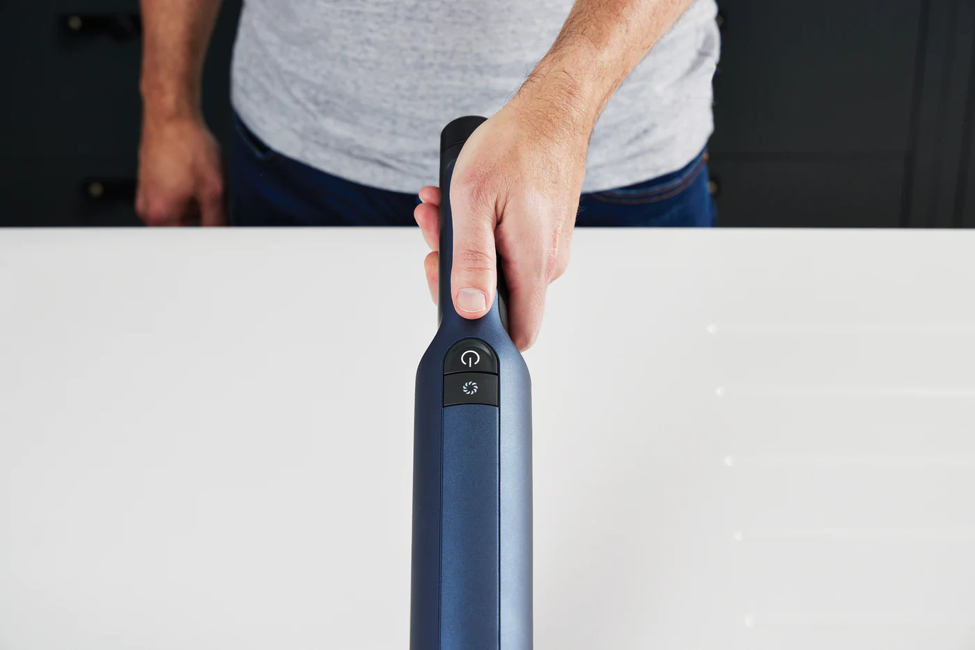 Main d'une personne tenant une poignée d'aspirateur bleu foncé, avec un bouton d'alimentation.