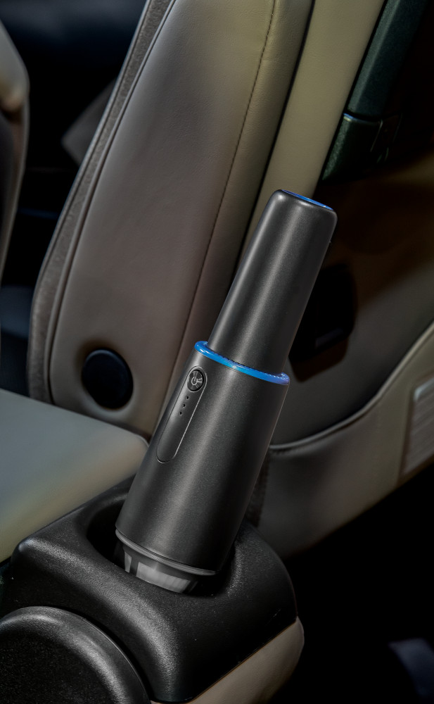 Un appareil noir avec des lumières bleues dans le porte-gobelet d'une voiture. Il est cylindrique et a un bouton.