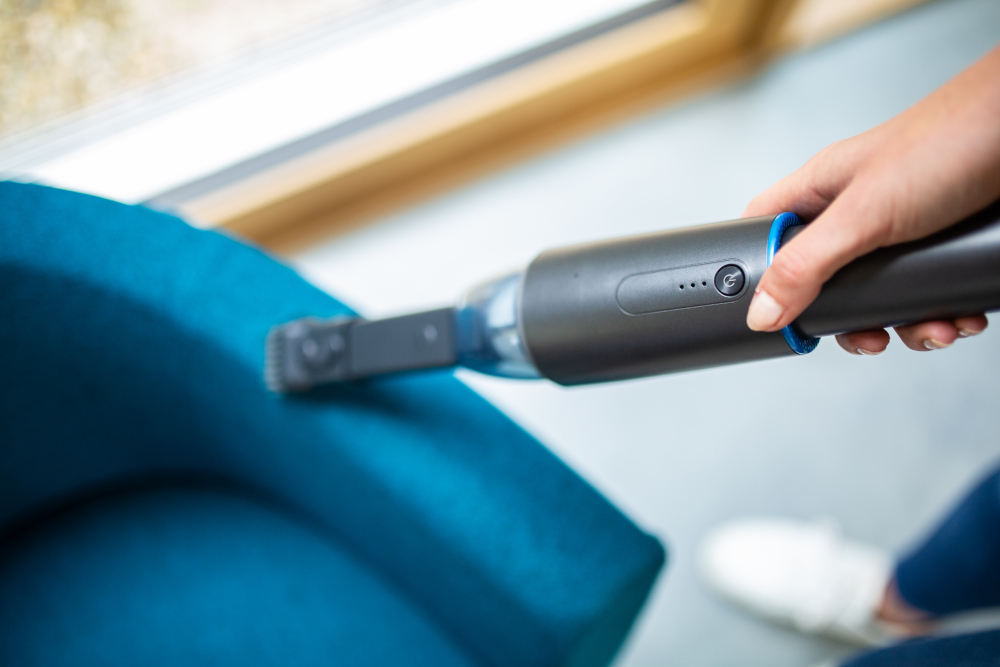 Une personne utilisant un aspirateur à main noir sur un canapé bleu.