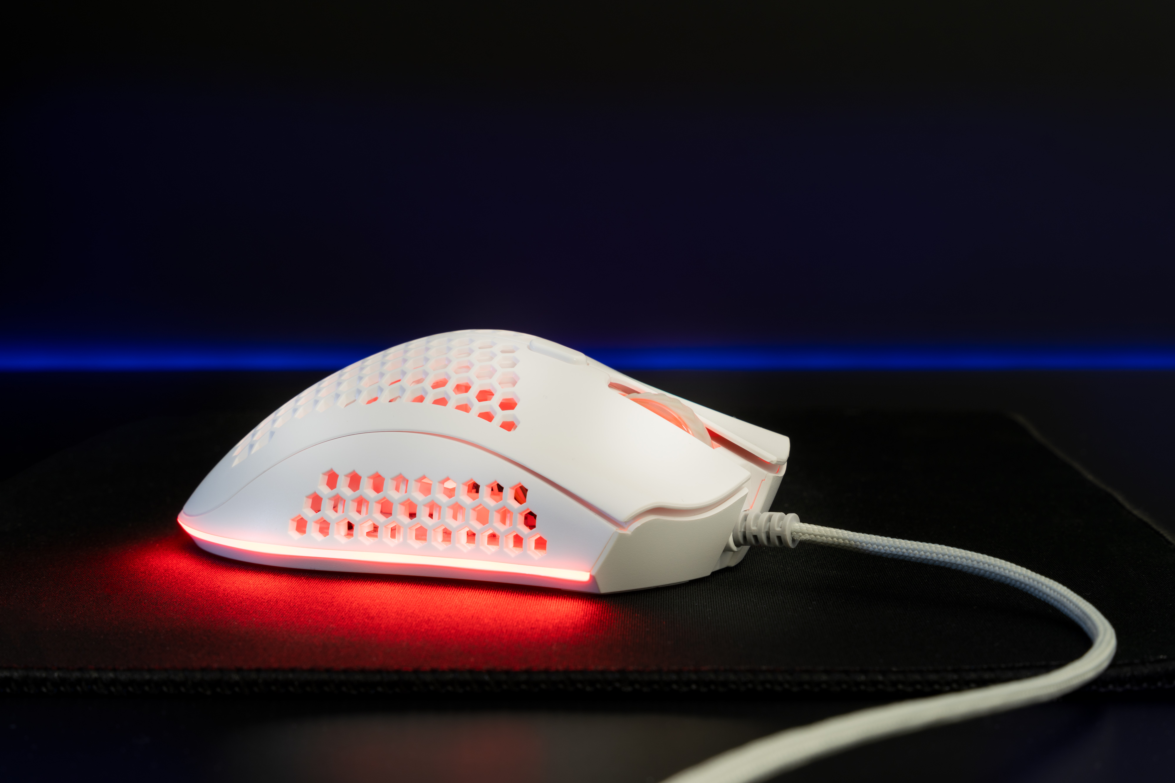 Eine weiße Gaming-Maus mit Wabenmuster und roten LED-Lichtern.