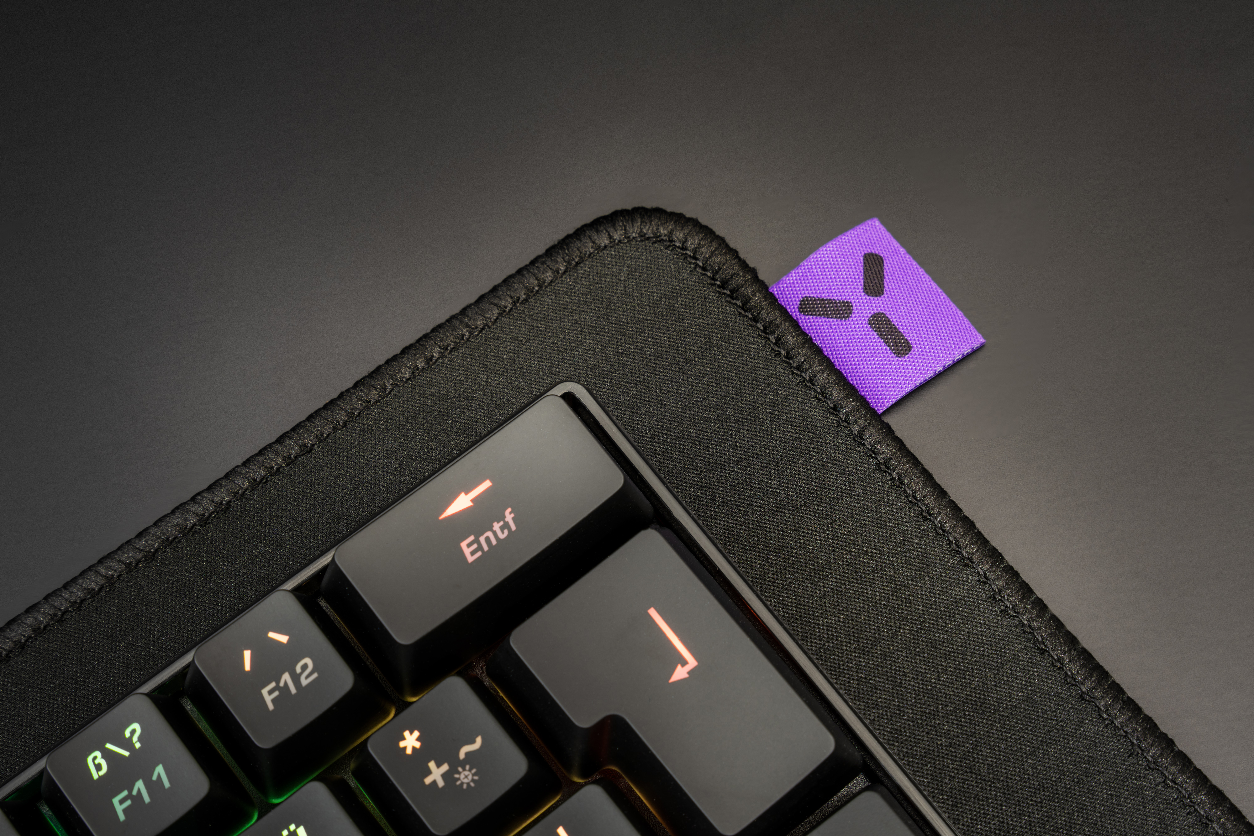 Tastatur mit lila Anhänger. Die 'Entf'-Taste ist hervorgehoben. Schwarze Oberfläche, Nahaufnahme.