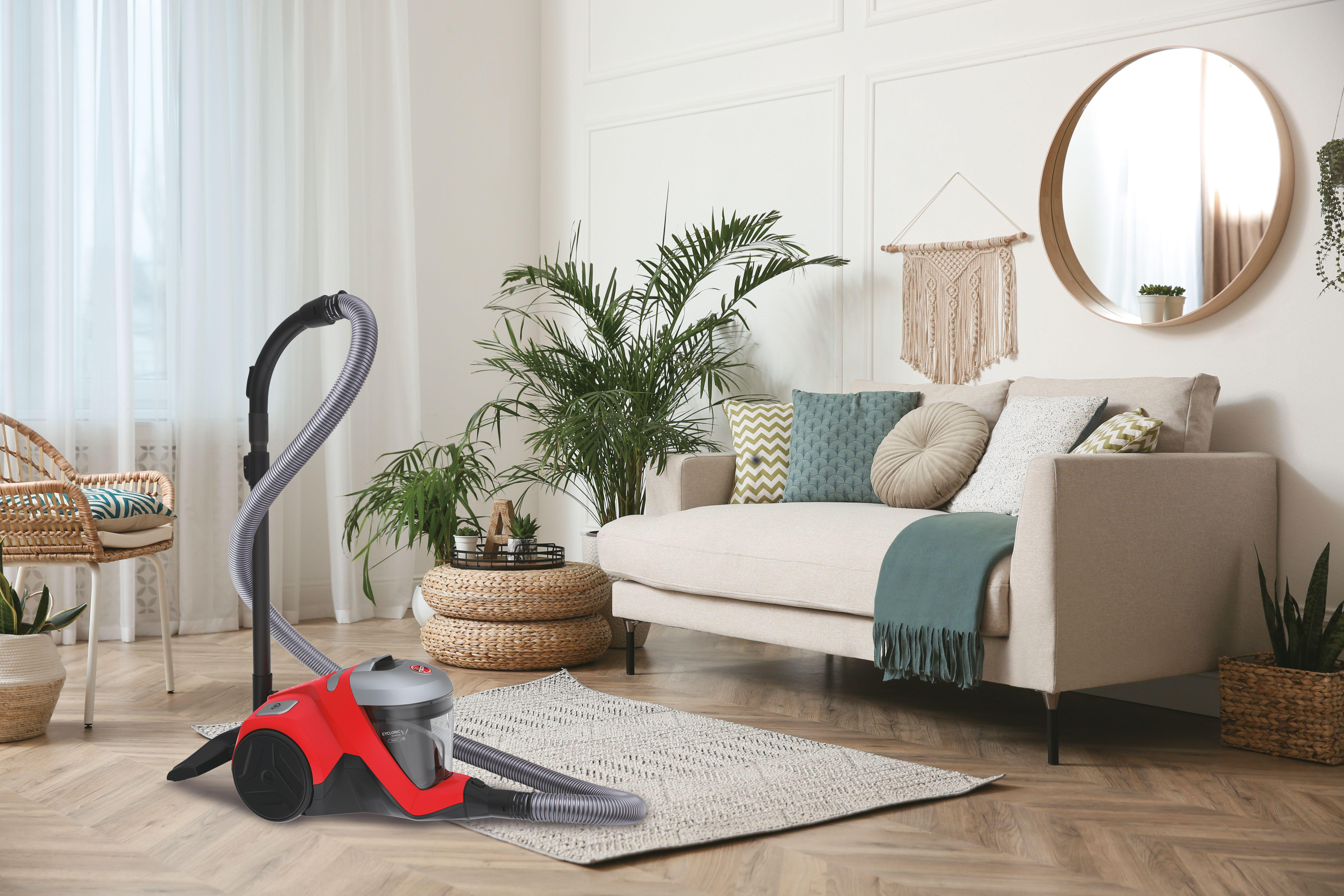Roter Staubsauger auf einem Teppich. Sofa, Pflanzen und Heimdekoration schaffen Wohnzimmerambiente.