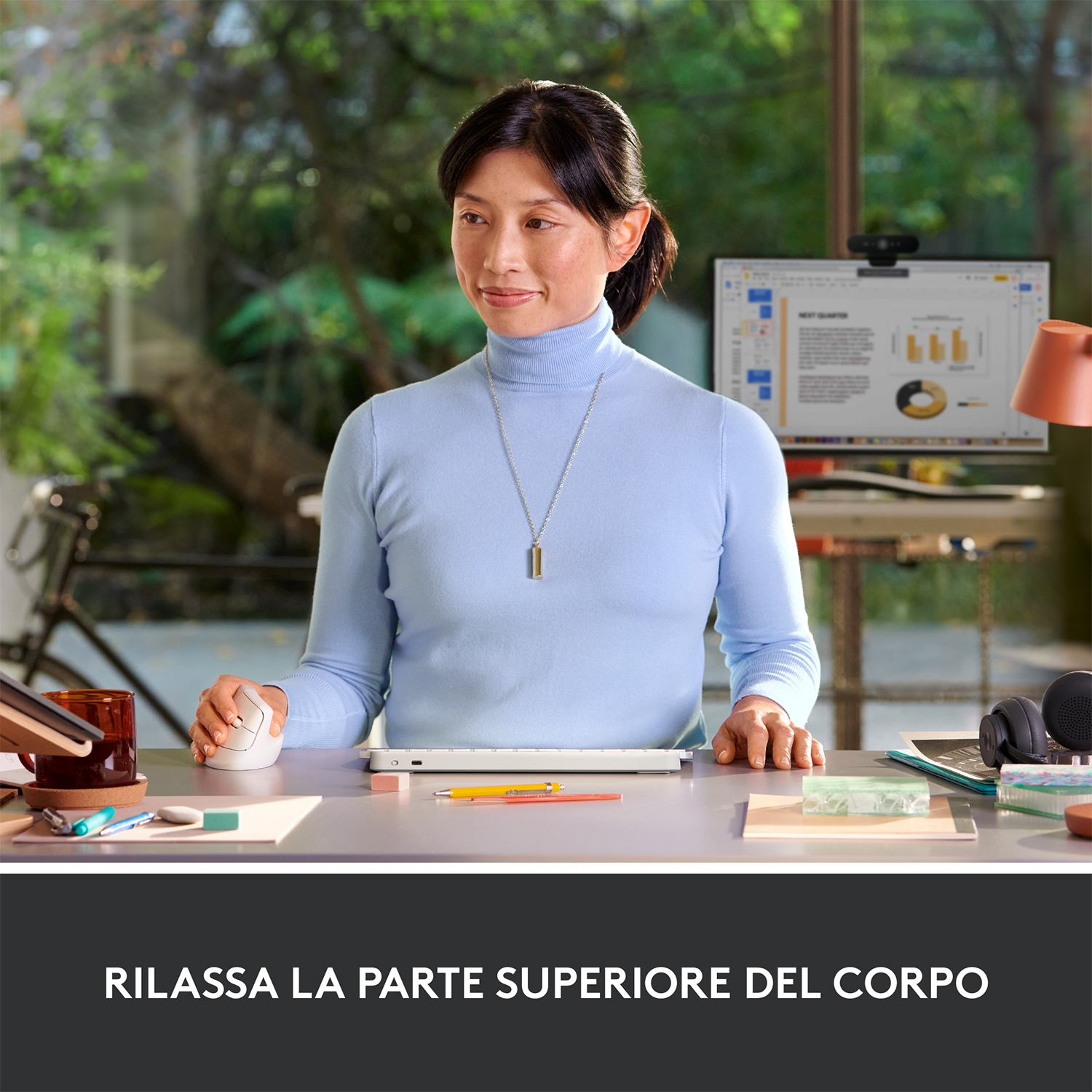 Una donna alla scrivania usa tastiera e mouse. Indossa un dolcevita blu.