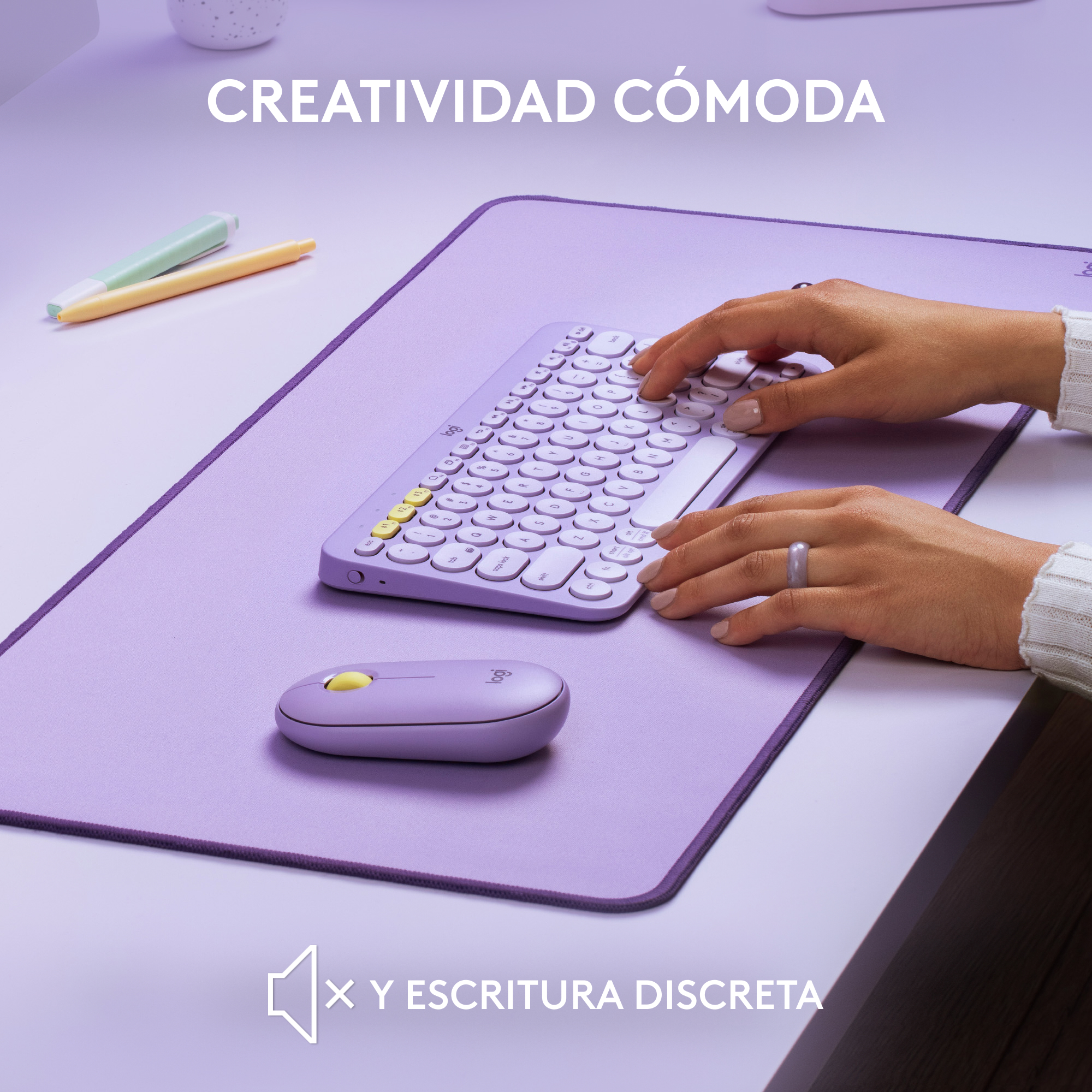 Manos escribiendo en teclado blanco compacto en escritorio morado, con ratón. Fondo: un bolígrafo.