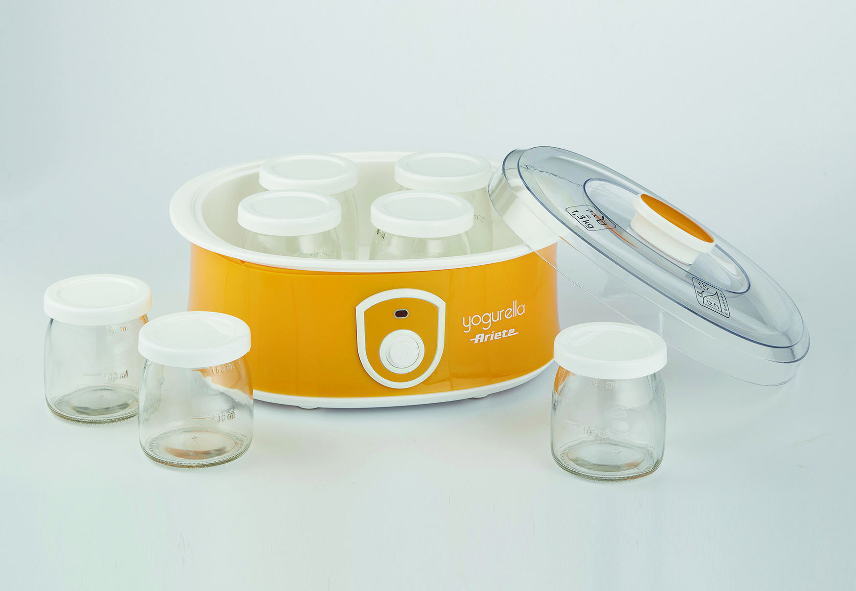 Una yogurtera amarilla con tarros de vidrio y una tapa transparente, dispuesta sobre una superficie blanca.