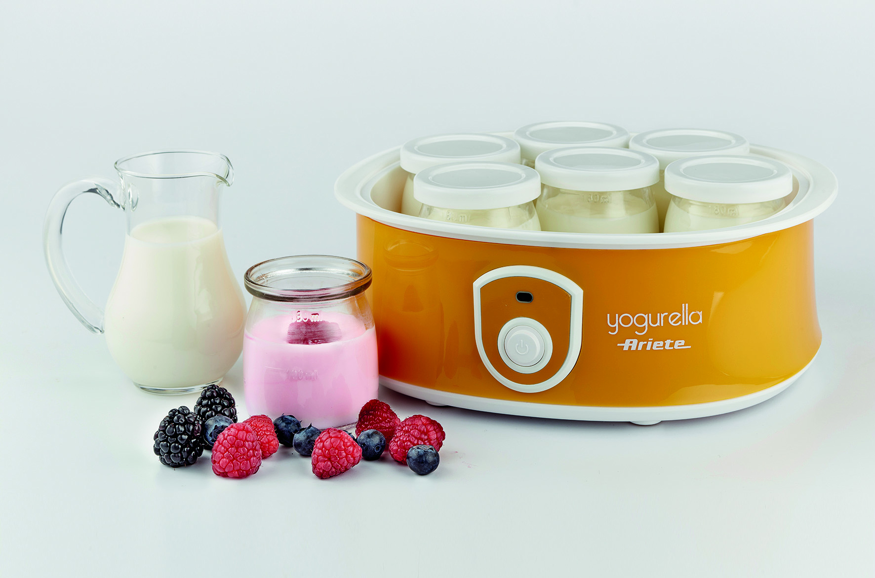 Yogurtera con frascos, jarra de leche y bayas frescas.