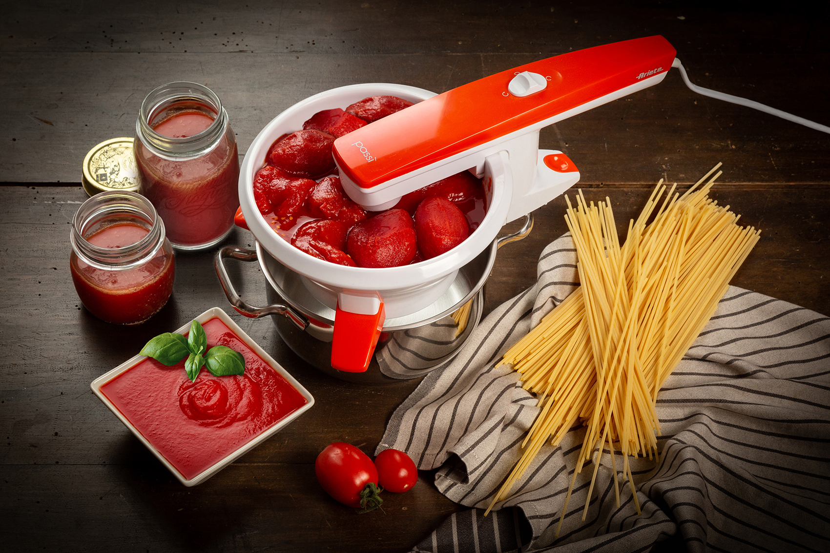 Máquina para procesar tomates. Tomates en una olla, frascos de salsa y pasta a un lado.
