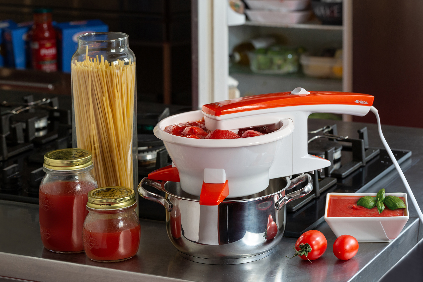 Escena de cocina con equipo de procesamiento de tomate. Se ven tomates, frascos de salsa y pasta.