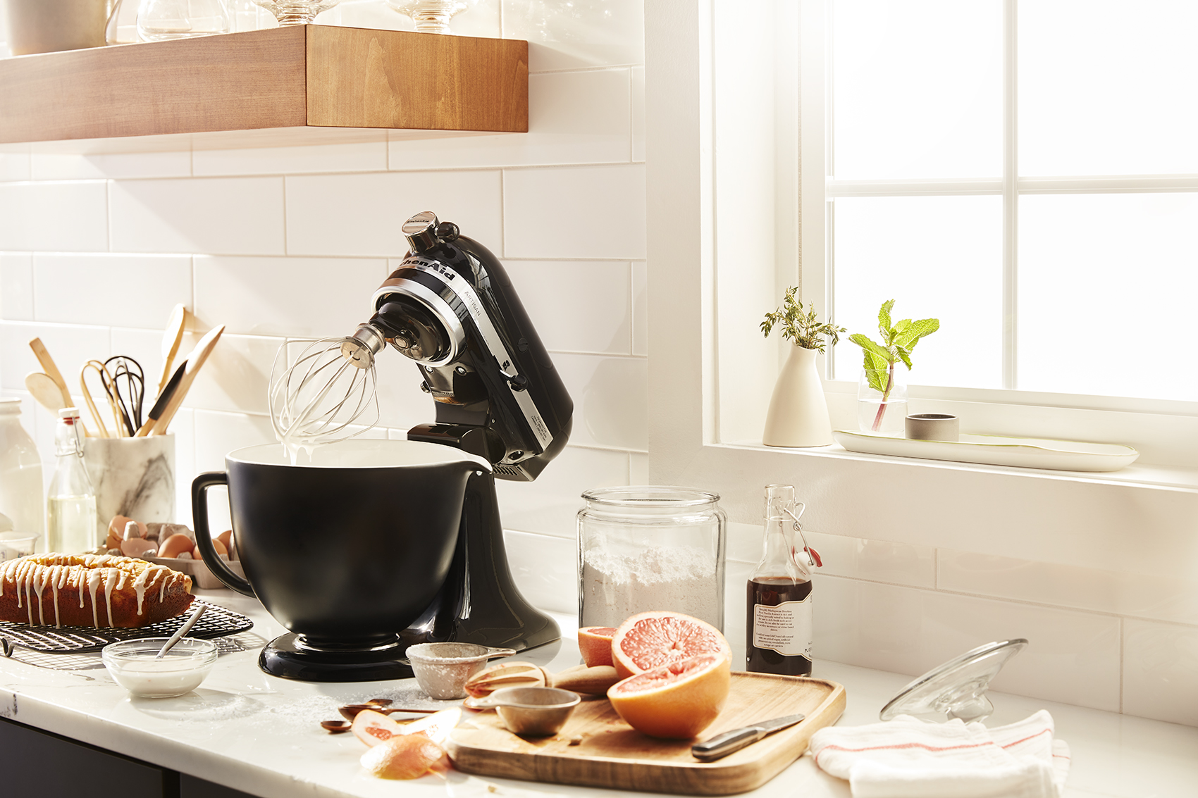 Una cocina con una batidora, ingredientes y una ventana.