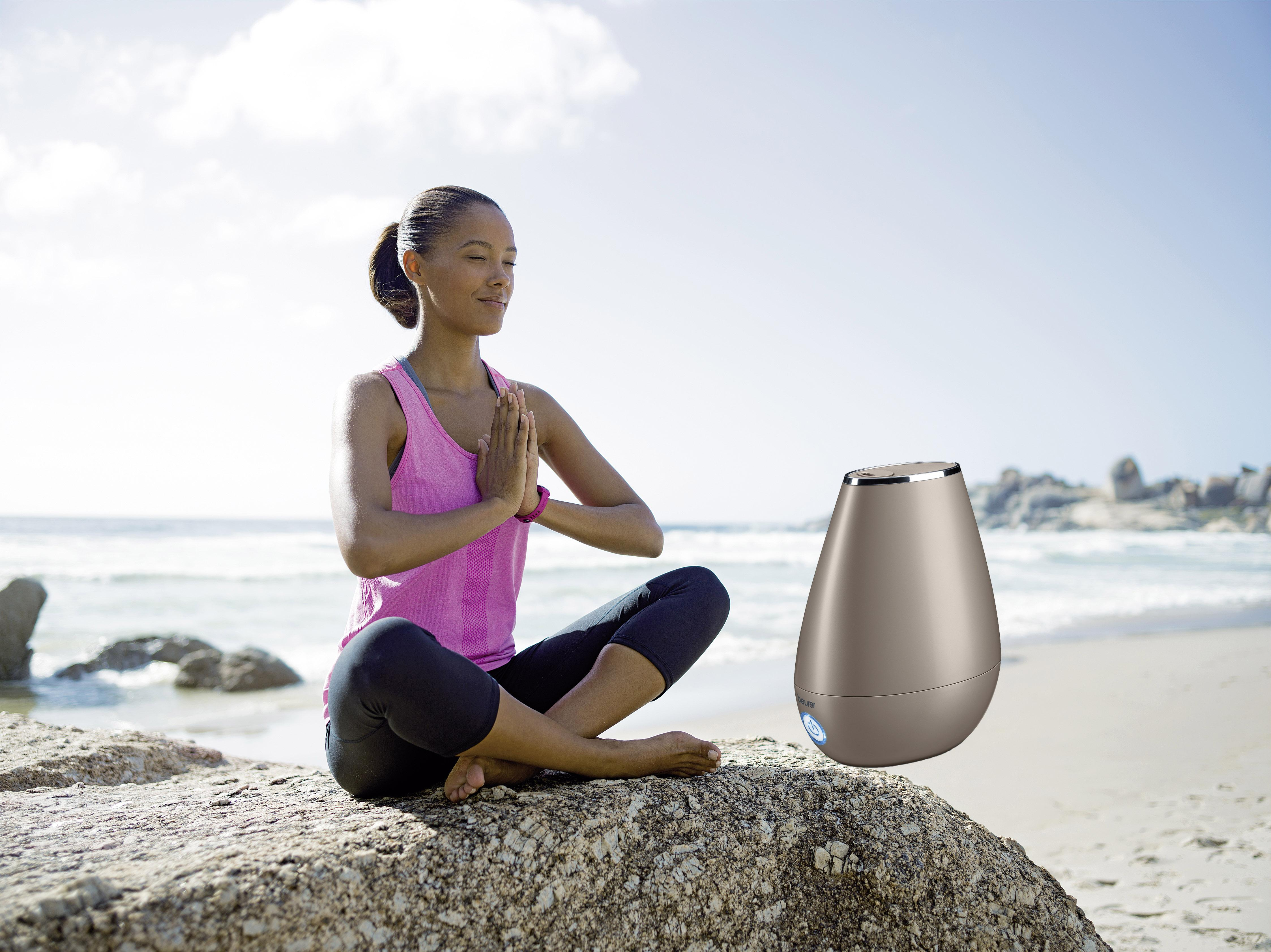 Una mujer medita en una playa con un humidificador a su lado.