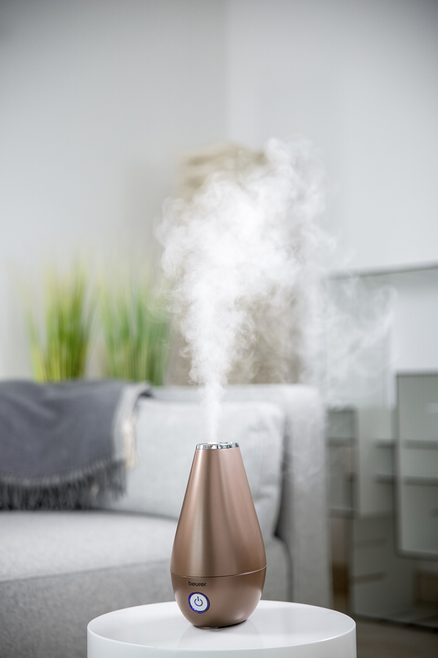 Un humidificador liberando vapor en una habitación. Está en una mesa con un sofá al fondo.